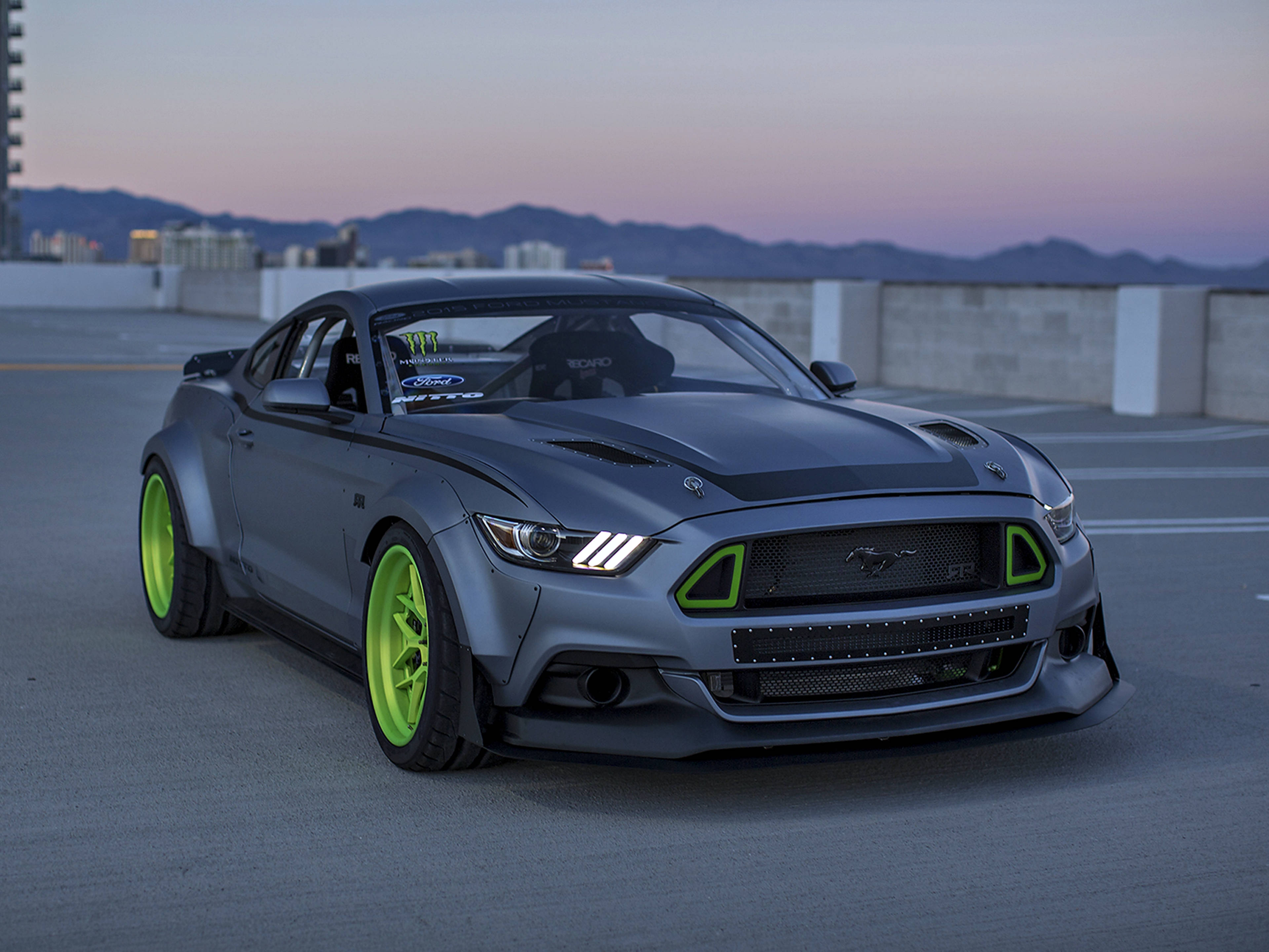 Ford Mustang 桌布 壁紙 — 一輛啞光灰色的福特野馬，配備螢光綠色車輪和裝飾，停泊在暮色中的屋頂上，背景有山脈。
