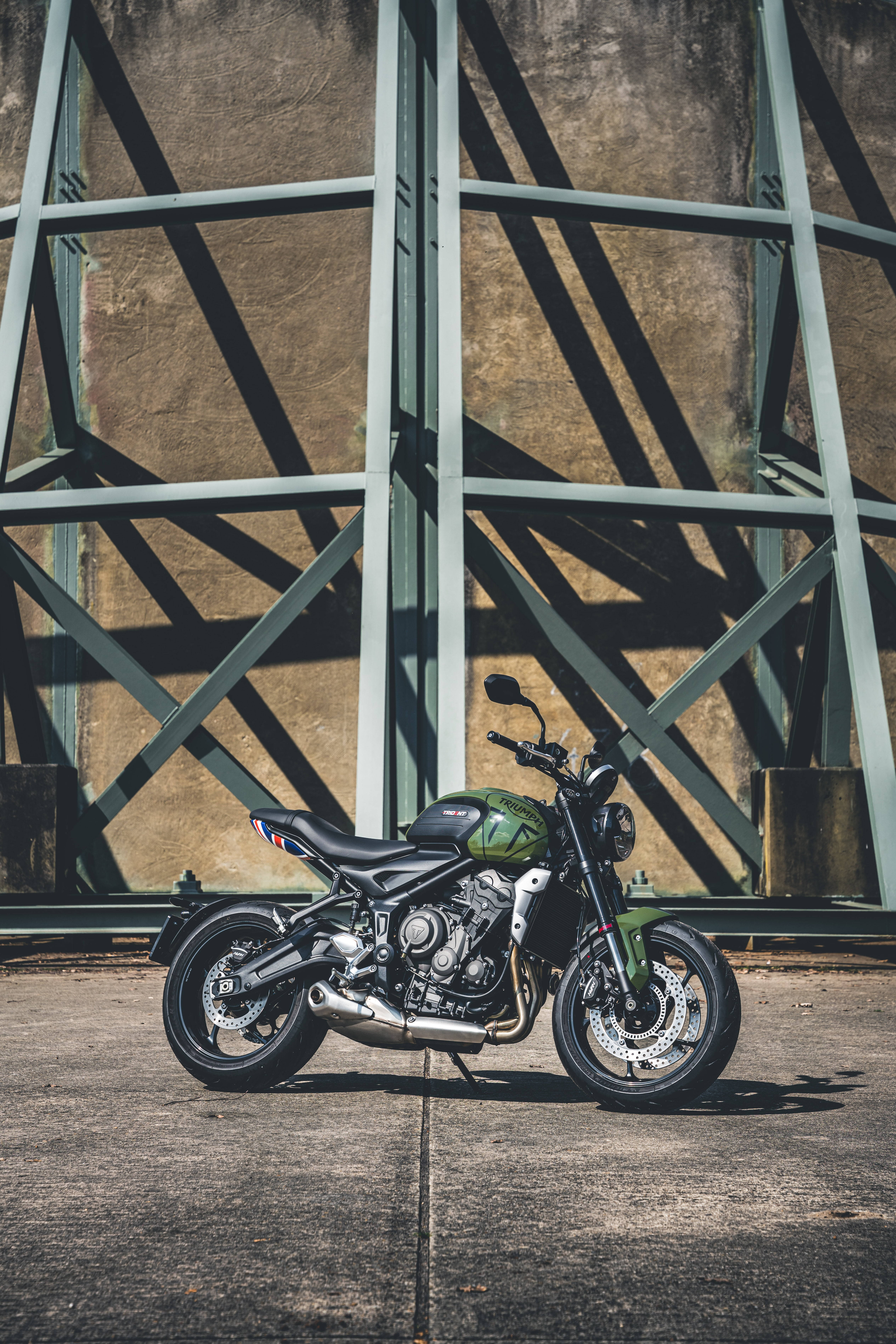 Bobber 桌布 壁紙 — 一輛啞光綠色摩托車在幾何鋼樑下擺好姿勢，鋼樑在混凝土上投下銳利的陰影。