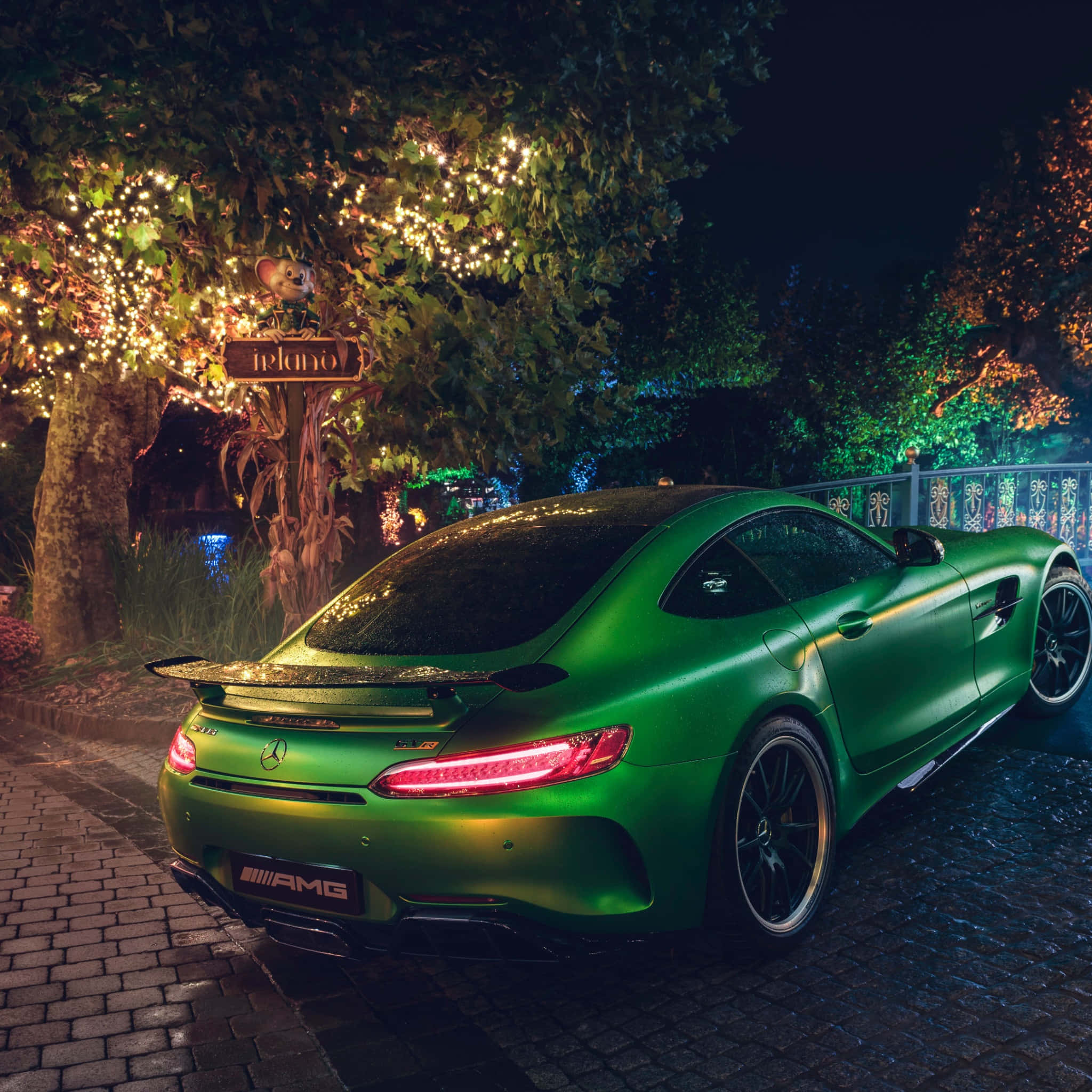 汽車 桌布 壁紙 — 一輛啞光綠色的 Mercedes-AMG GT 在夜晚停泊在發光的串燈下，位於鵝卵石小徑上。