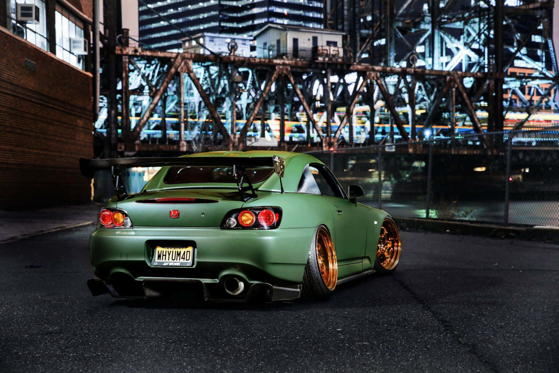 Honda S2000 桌布 壁紙 — 一輛啞光綠色的改裝跑車配金色輪圈，夜晚停泊在工業橋下，城市環境中。