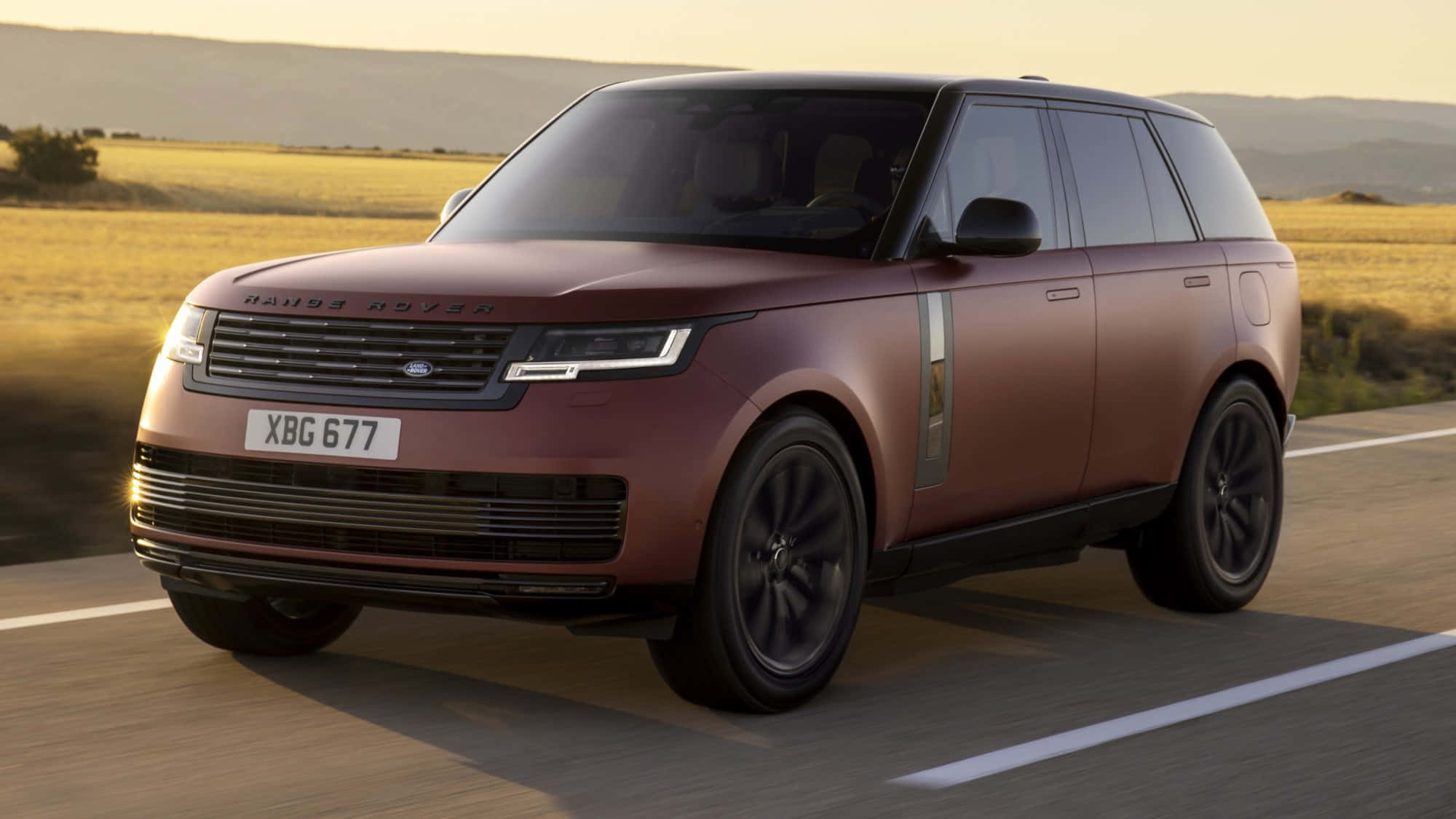 Range Rover 桌布 壁紙 — 一輛啞光酒紅色的Range Rover SUV在陽光明媚的鄉村道路上行駛，背景是金色的山丘。
