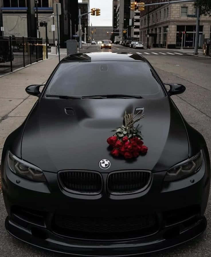 Bmw m5 壁紙 — 一輛啞光黑色BMW M3，引擎蓋上放著一束紅玫瑰，停泊在城市的街道上。