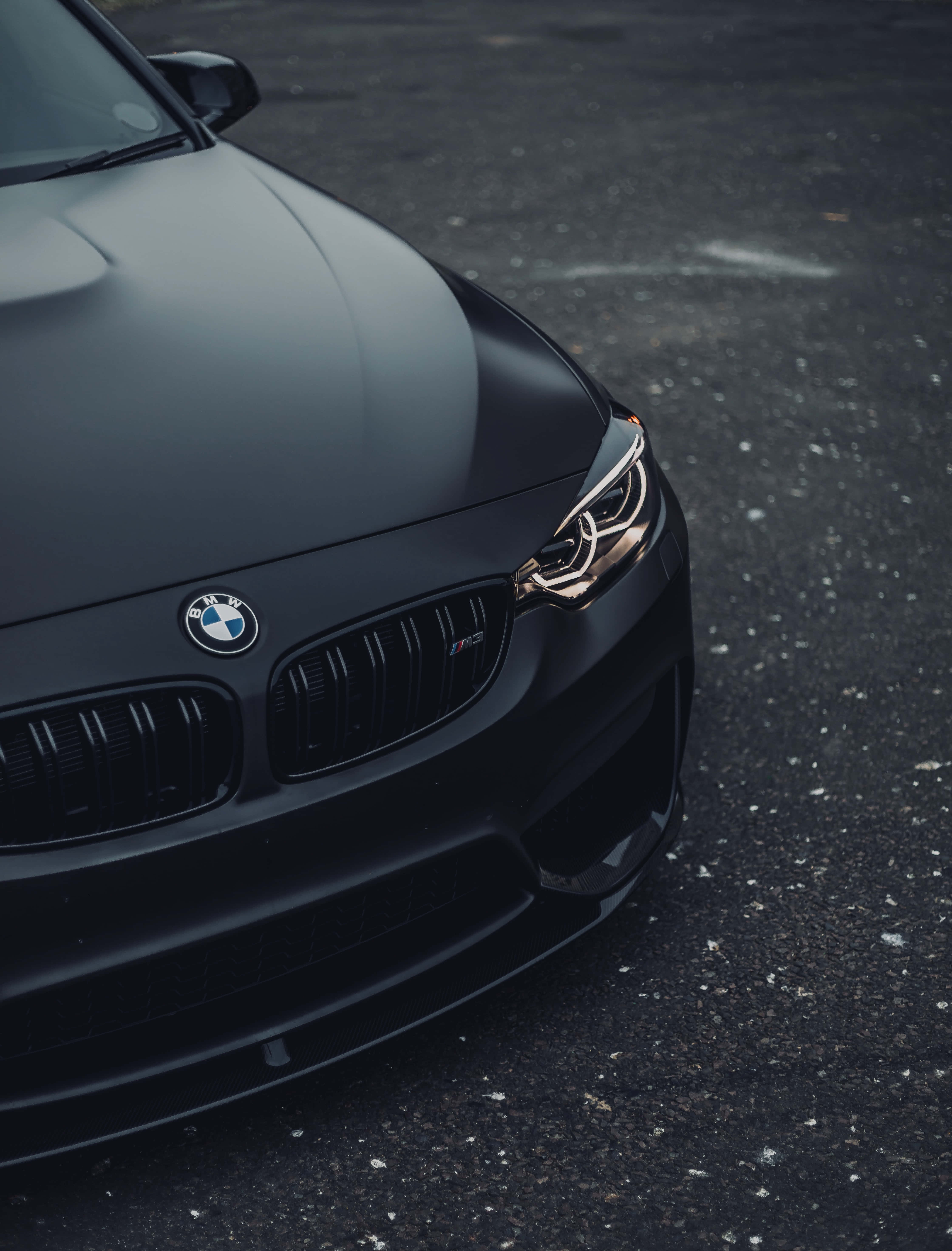 BMW 動圖 桌布 壁紙 — 一輛啞光黑色BMW M3跑車停在瀝青路面上，金色頭燈閃爍。