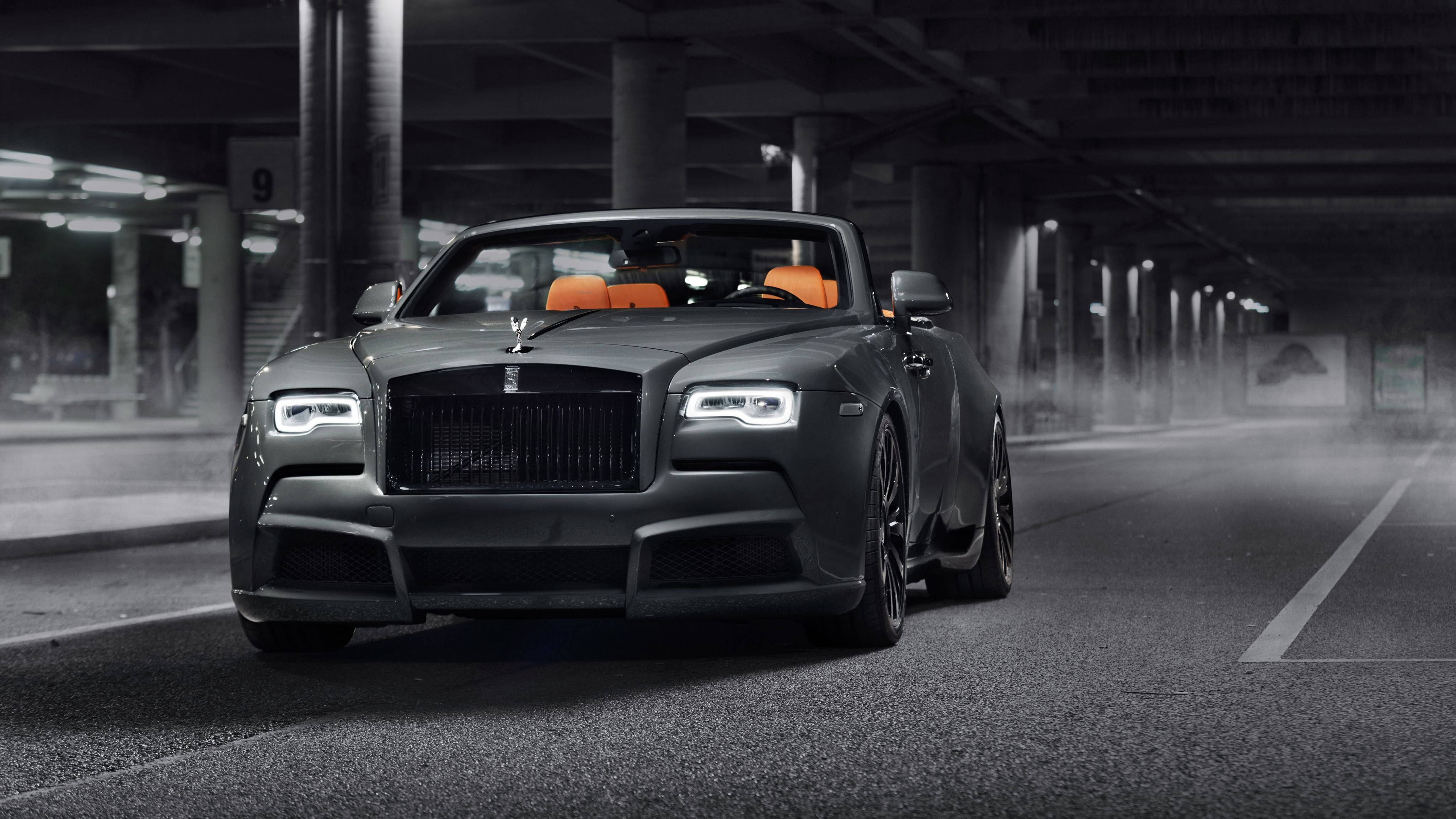 Royce 桌布 壁紙 — 一輛啞光黑色勞斯萊斯敞篷車配橙色座椅，在人工燈光下穿過霧氣瀰漫的地下停車場。