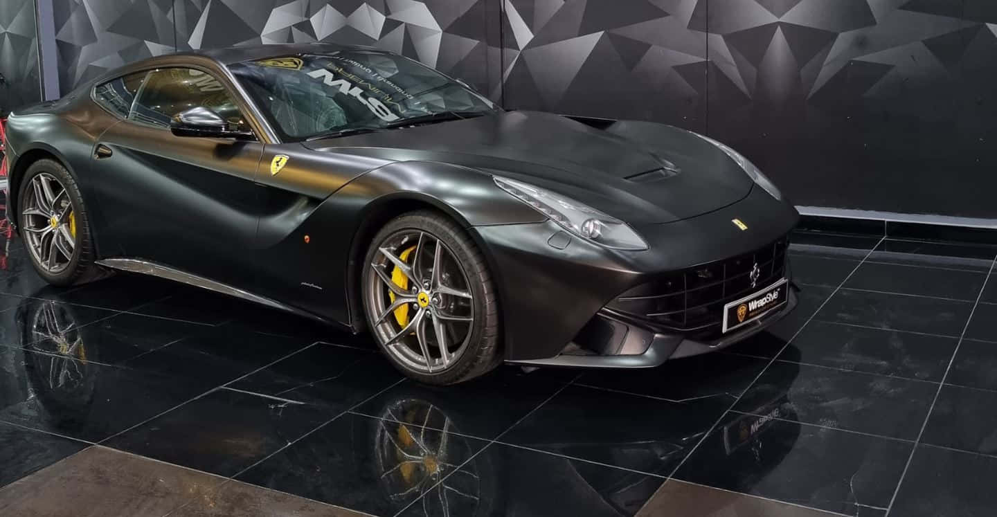 Ferrari F12 Berlinetta 桌布 壁紙 — 一輛啞光黑色法拉利F12tdf跑車配黃色制動卡鉗，展示在亮面黑色瓷磚地板上，背景為幾何牆壁。