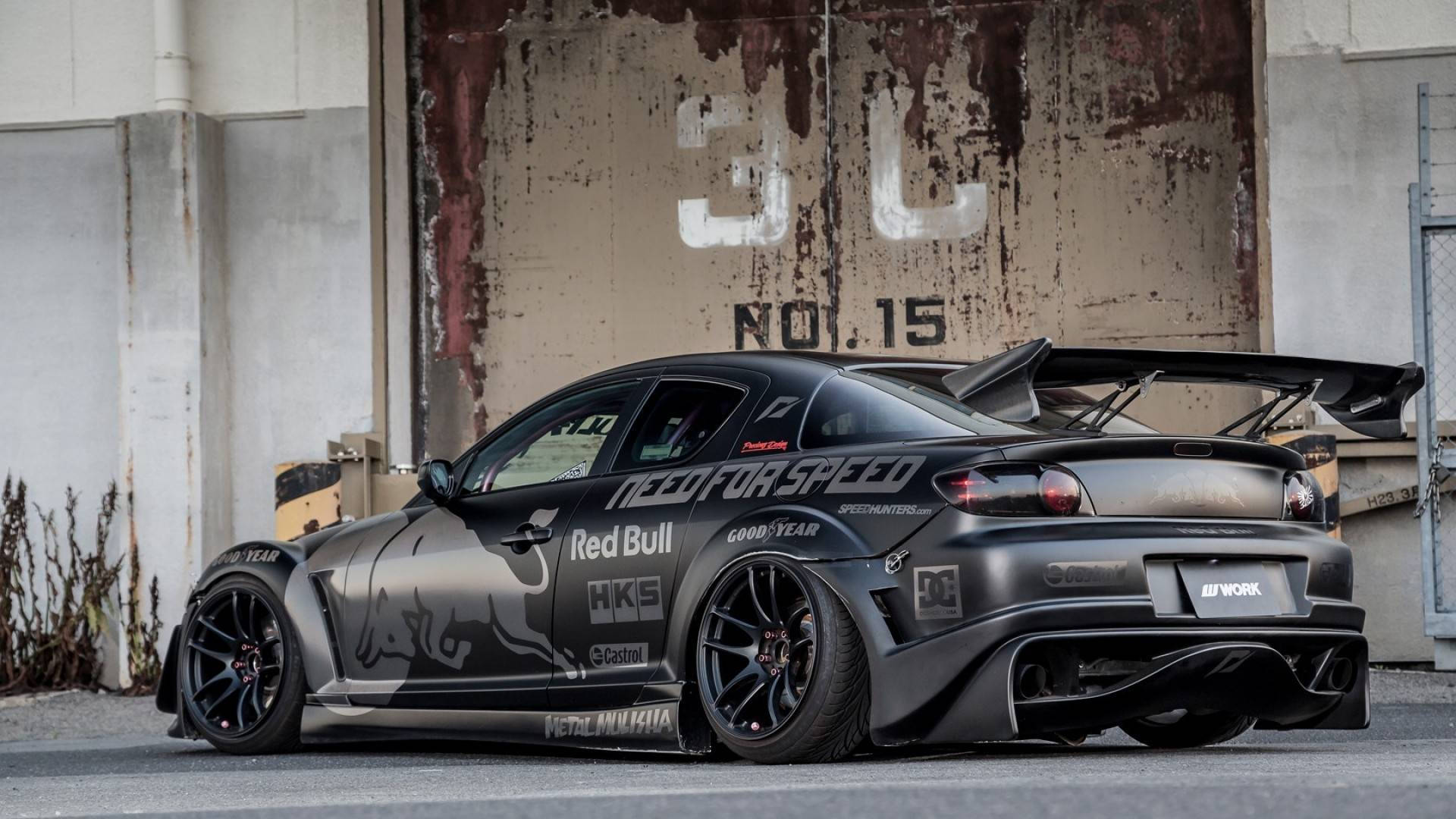 Mazda 桌布 壁紙 — 一輛啞光黑色的馬自達RX-7飄移車，帶有Red Bull和Need for Speed貼紙，停在風化的工業牆前。