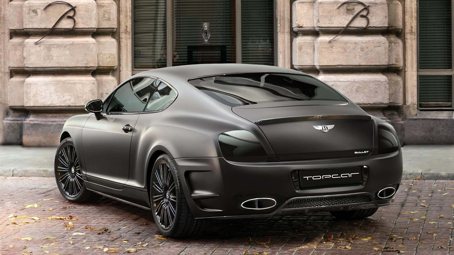桌布 壁紙 — 一輛啞光黑色賓利 Continental GT 停泊在散落著秋葉的磚砌街道上。