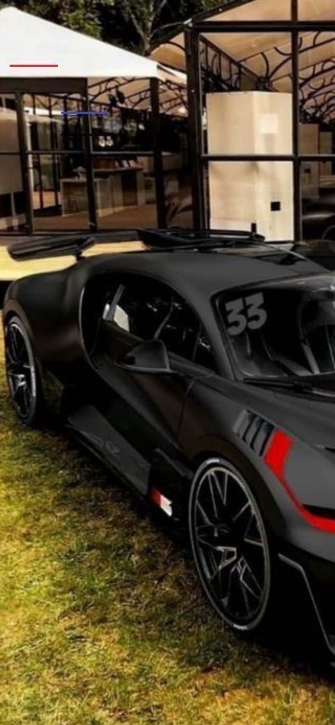 iPhone Xs Bugatti 桌布 壁紙 — 一輛啞光黑色跑車帶有紅色點綴和號碼33，停在現代玻璃建築附近的草地上。