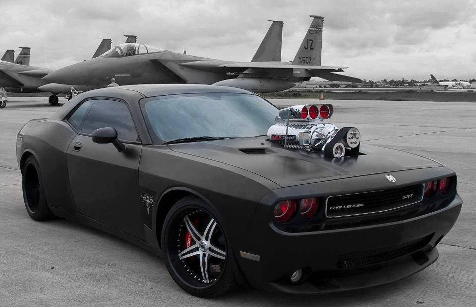 Challenger 桌布 壁紙 — 一輛啞黑色Dodge Challenger SRT配備鍍鉻增壓器，停在陰天下的機場跑道上，旁邊有戰鬥機。