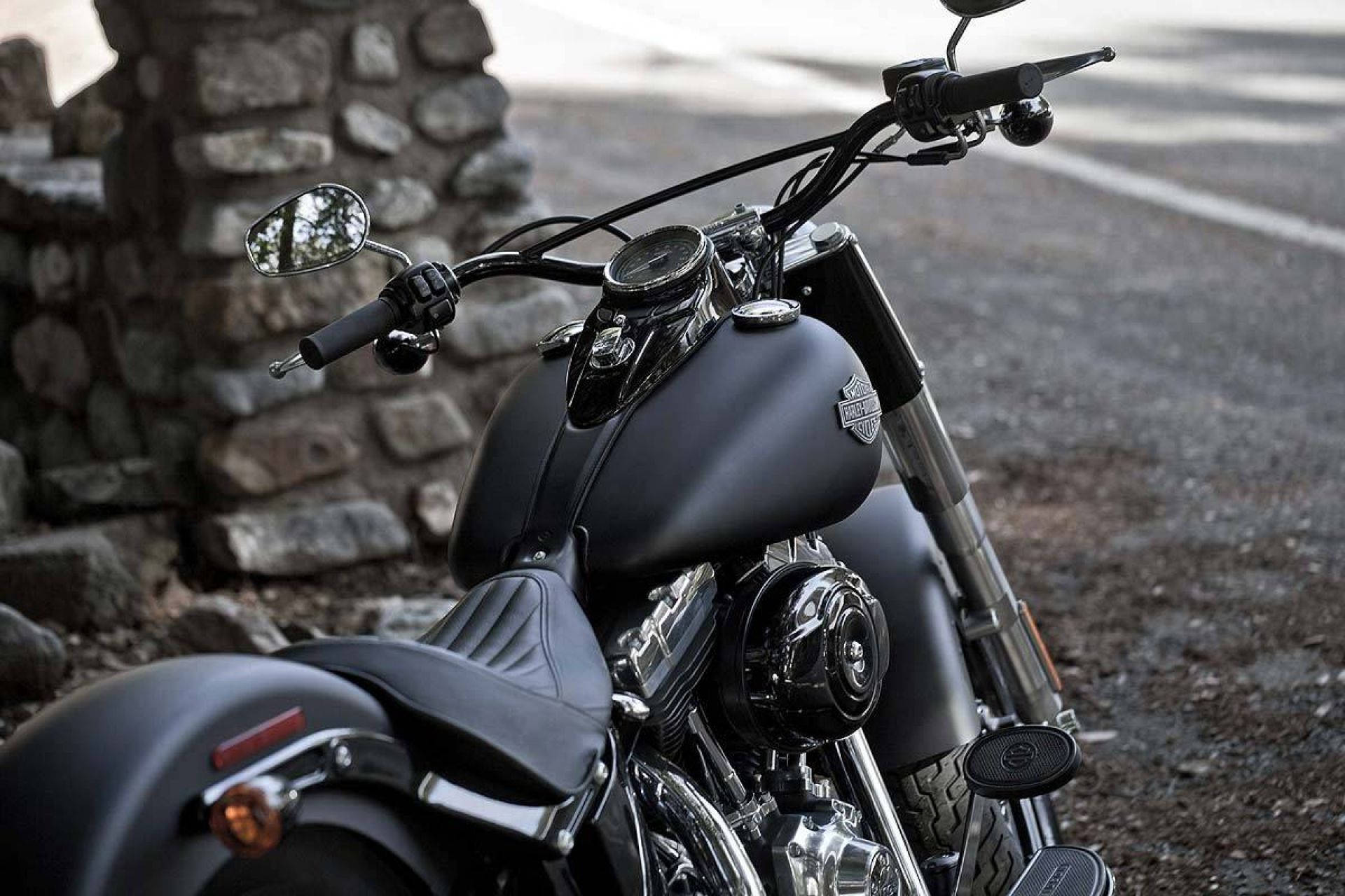 Harley 桌布 壁紙 — 一輛啞黑色哈雷戴維森機車帶有鍍鉻裝飾，停放在碎石路邊的石牆旁。