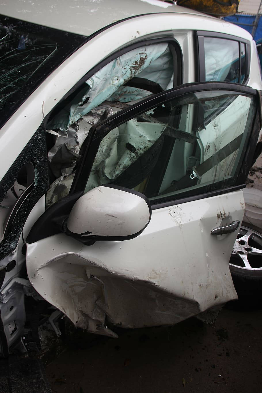 car crash 桌布 壁紙 — 一輛嚴重損壞的白色汽車，車窗破碎，前門被壓碎，停在廢車場。