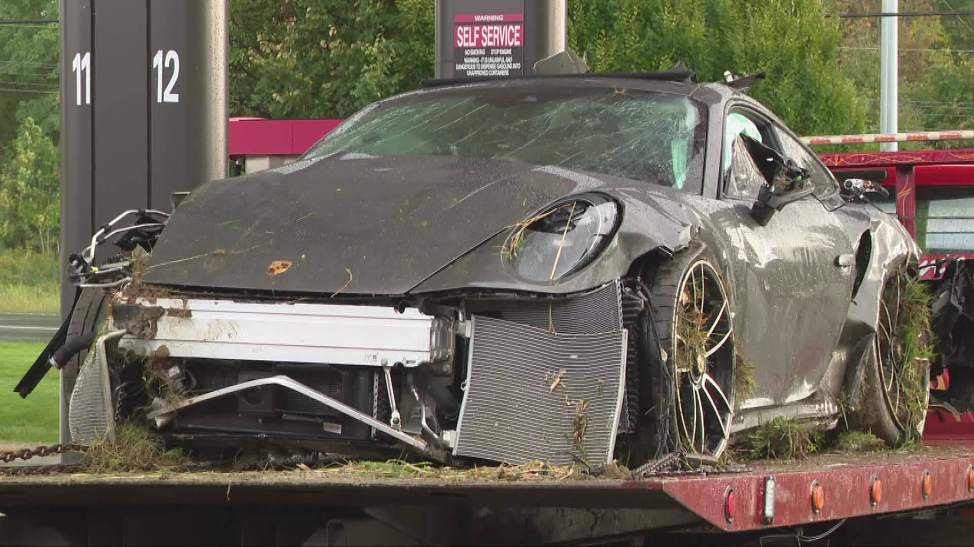 車禍 桌布 壁紙 — 一輛嚴重損毀、覆蓋著草叢的黑色保時捷跑車，停放在加油站的紅色拖車上。