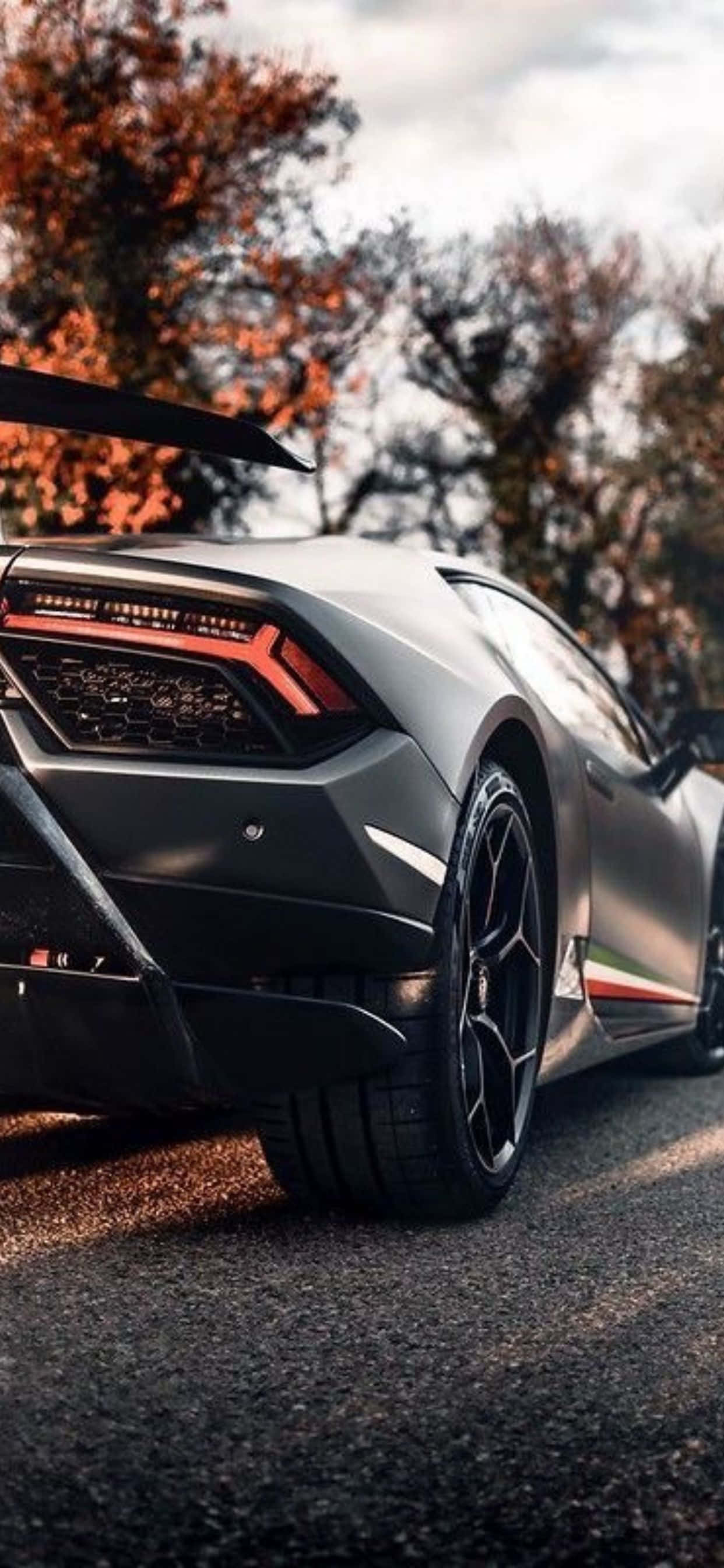 Lamborghini Phone 桌布 壁紙 — 一輛型格啞光灰色藍寶堅尼 Huracán Performante 停在柏油路上，背後秋樹在溫暖光線中閃耀。