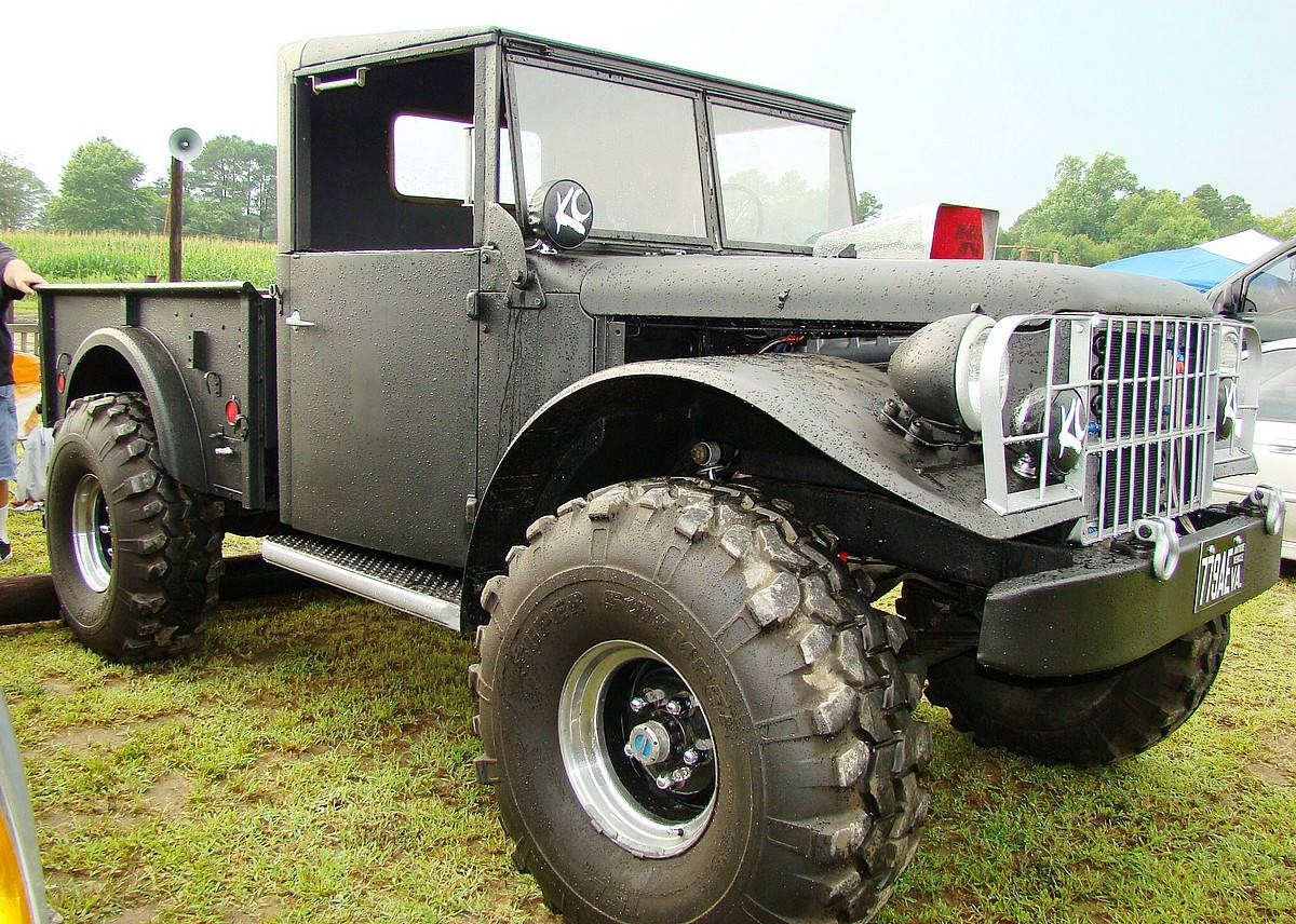 Trucks 桌布 壁紙 — 一輛堅固的啞光黑色復古軍用卡車，配備巨大的越野輪胎，停泊在陰天下的草地上。