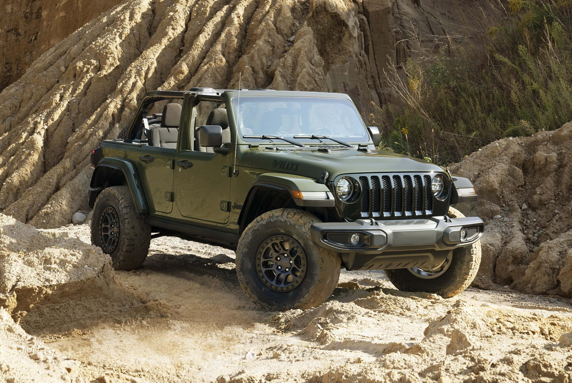 吉普 桌布 壁紙 — 一輛堅固的橄欖綠色Jeep Wrangler在明亮的日光下，沿著質感岩石 formations 旁邊的陡峭沙坡行駛。