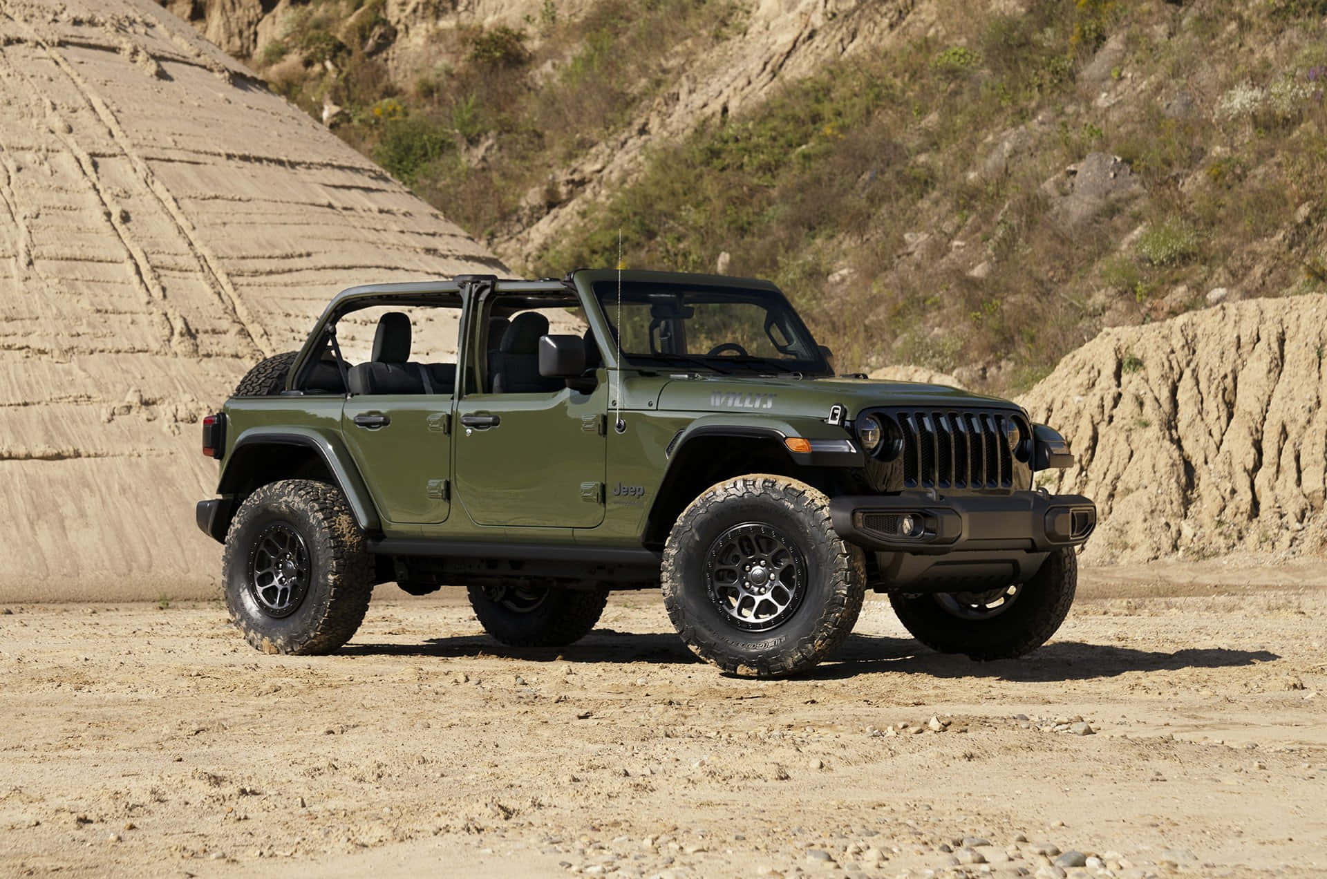吉普 桌布 壁紙 — 一輛堅固的橄欖綠色Jeep Wrangler配黑色輪胎，停在塵土飛揚的地形上，旁邊是層狀岩石結構，在明亮的日光下。