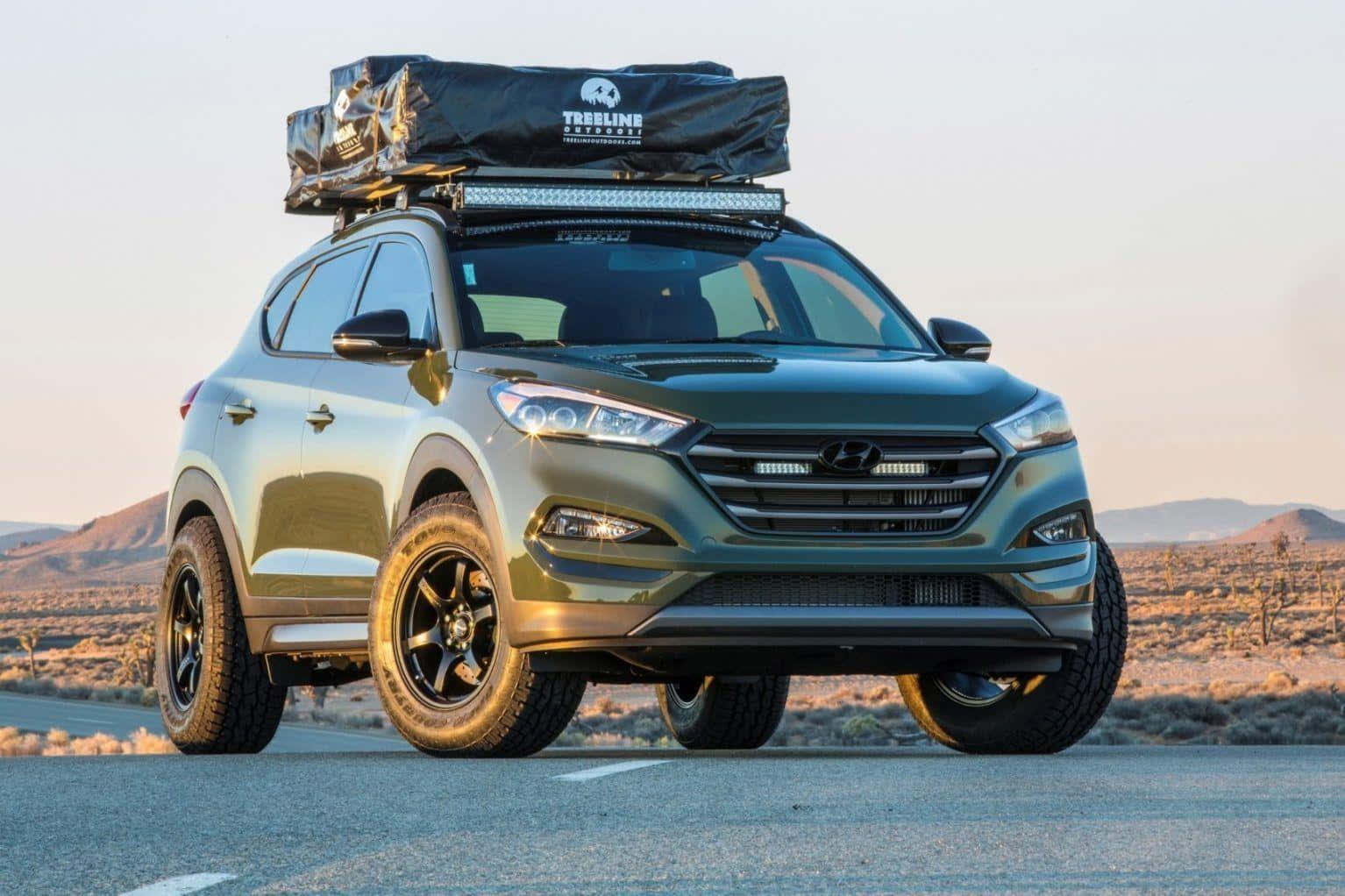 Hyundai Tucson 桌布 壁紙 — 一輛堅固的橄欖綠色SUV，配備黑色車輪和車頂行李架，停泊在沙漠公路上的黃金時刻。