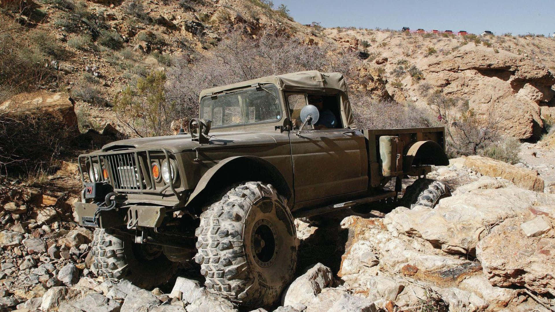 Jeep Gladiator 桌布 壁紙 — 一輛堅固的橄欖綠軍用卡車，配備巨型輪胎，在明亮的日光下攀爬陡峭的岩石地形。