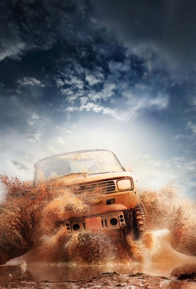Dirty 桌布 壁紙 — 一輛堅固的橙色越野車在泥濘地形中疾馳，在戲劇性的多雲天空下濺起棕色的水和泥土。