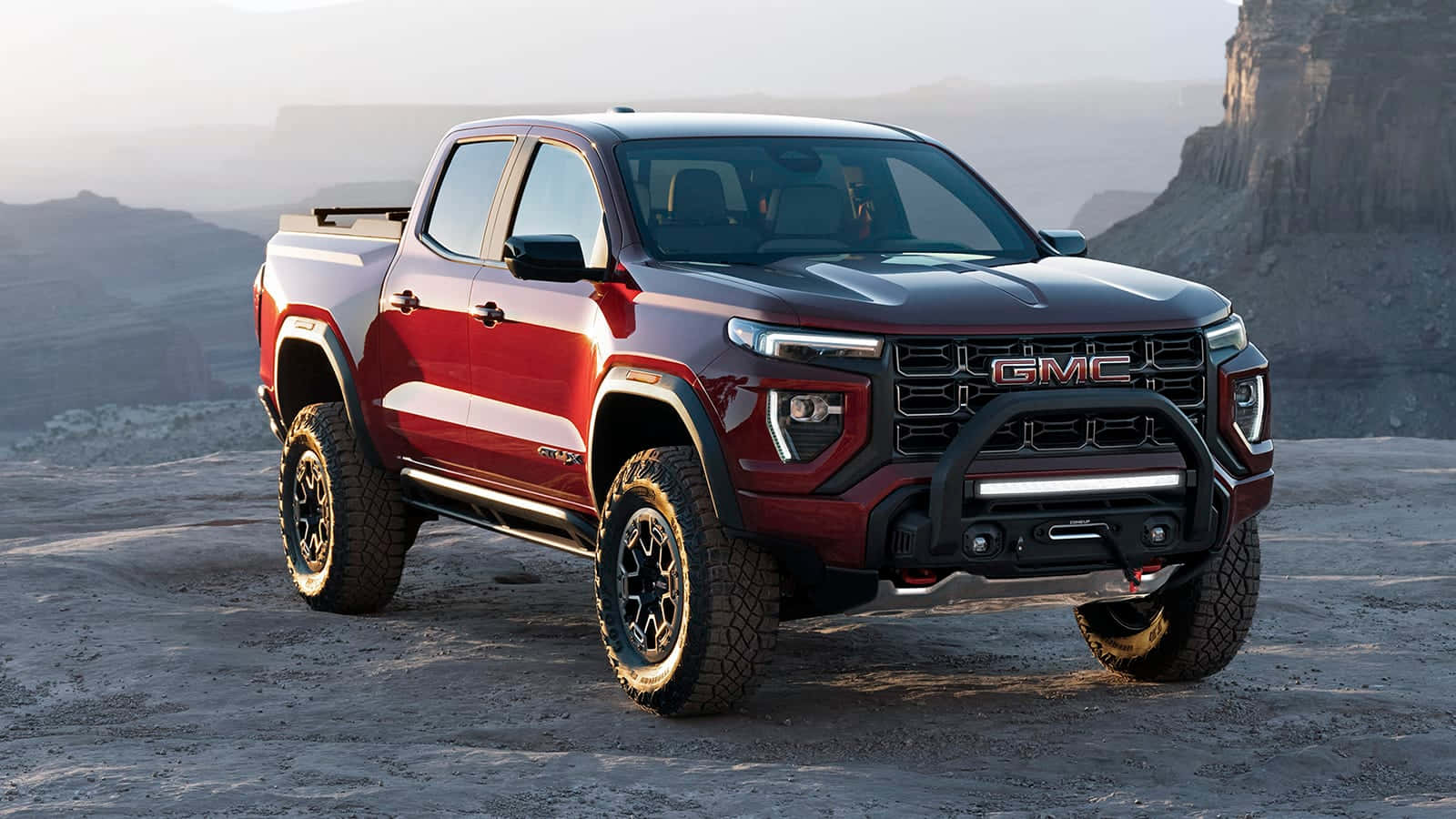 Gmc Canyon 桌布 壁紙 — 一輛堅固的紅色GMC Sierra AT4 pickup卡車停泊在塵土飛揚的沙漠高原上，背景是朦朧的岩石懸崖。