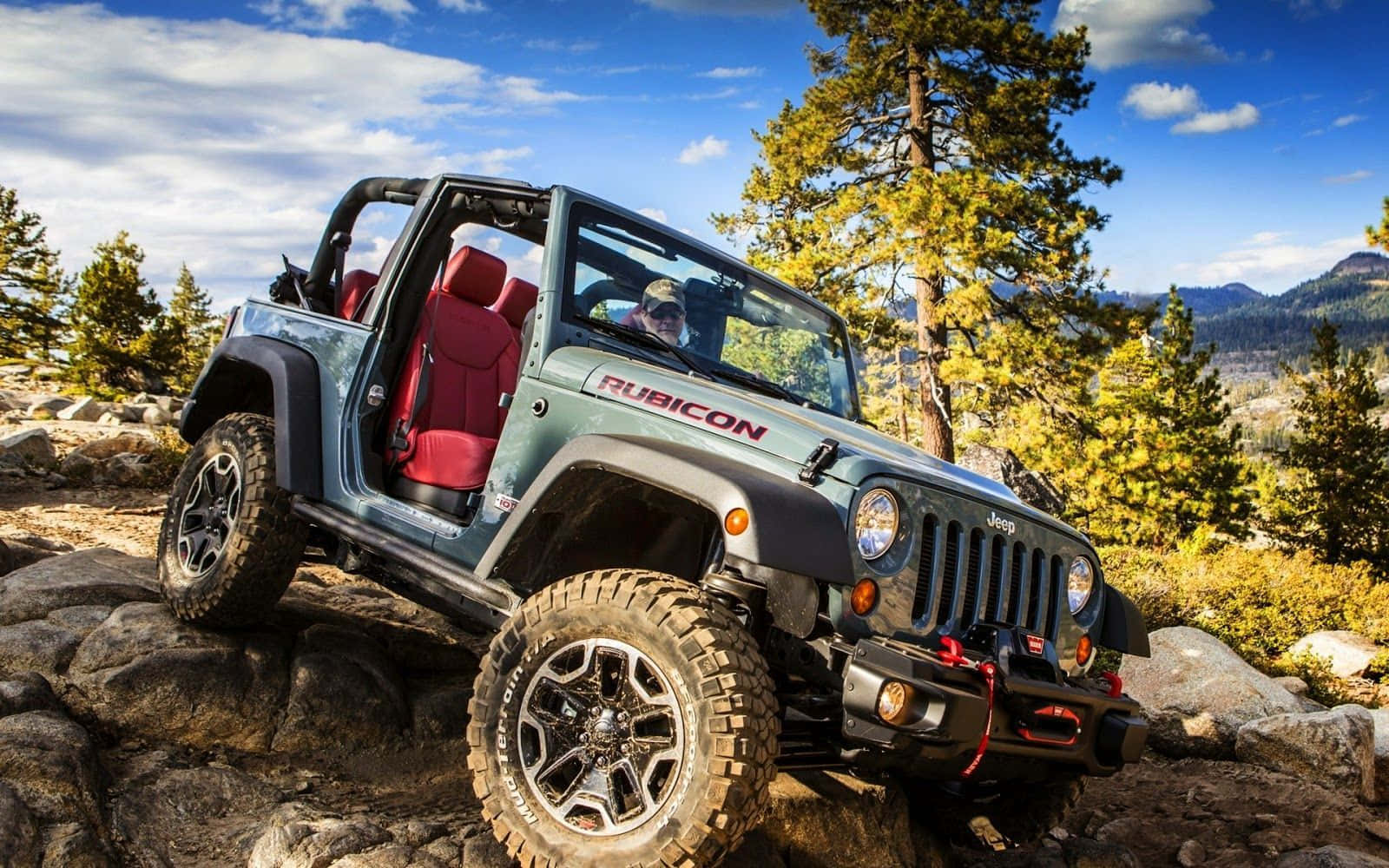 Jeep Cj 桌布 壁紙 — 一輛堅固的綠色Jeep Rubicon配紅色座椅，在點綴著白雲的明亮藍天下攀爬岩石地形。