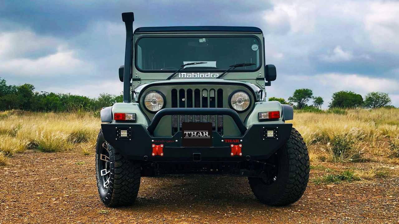 高清 桌布 壁紙 — 一輛堅固的綠色Mahindra Thar SUV正面朝向泥路，天空多雲，背景有乾草和稀疏樹木。