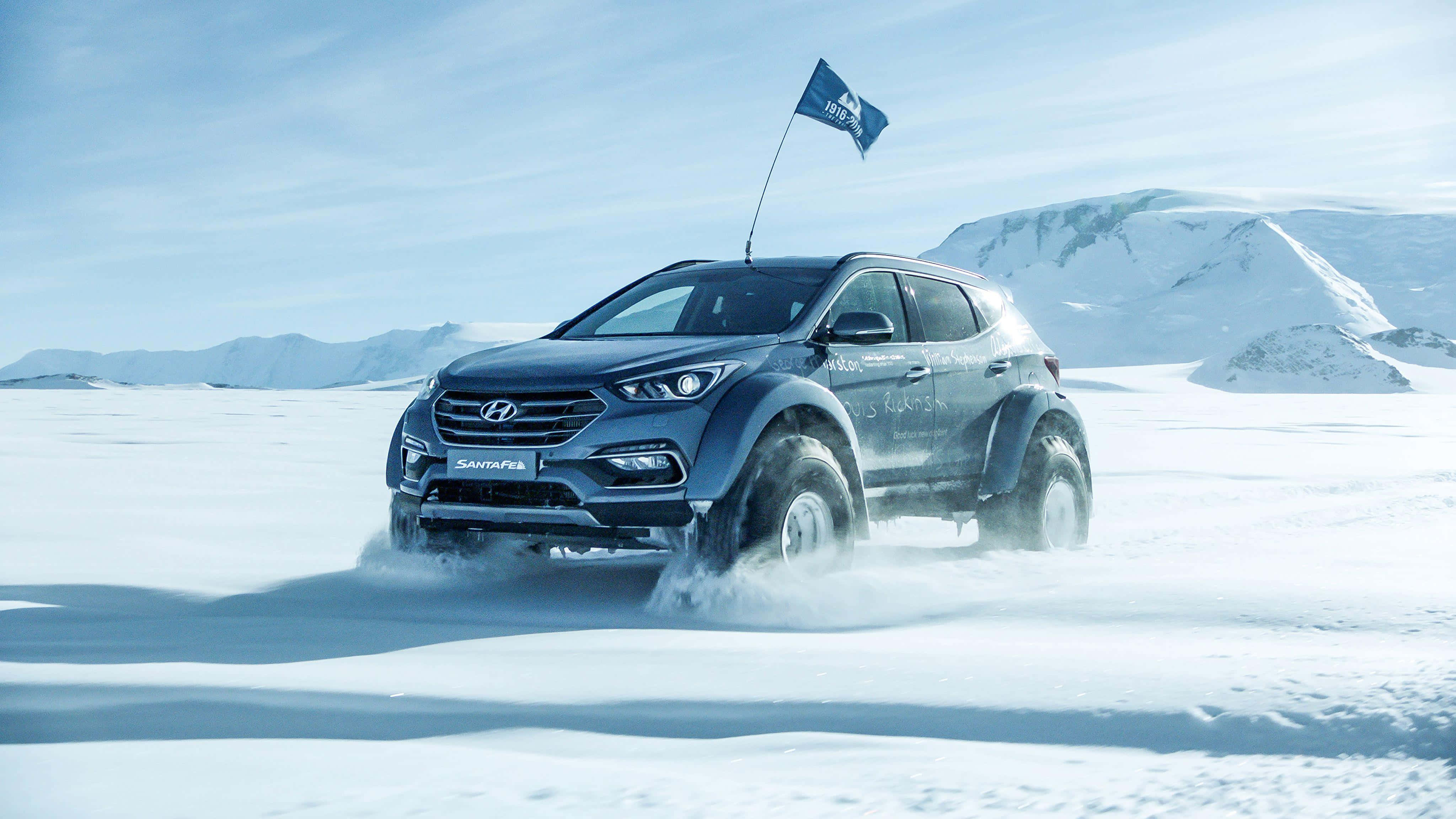 Hyundai Santa Fe 桌布 壁紙 — 一輛堅固的藍色現代Santa Fe SUV在深雪中行駛，車頂上旗幟飄揚，背景是藍天白雲下的雪山。