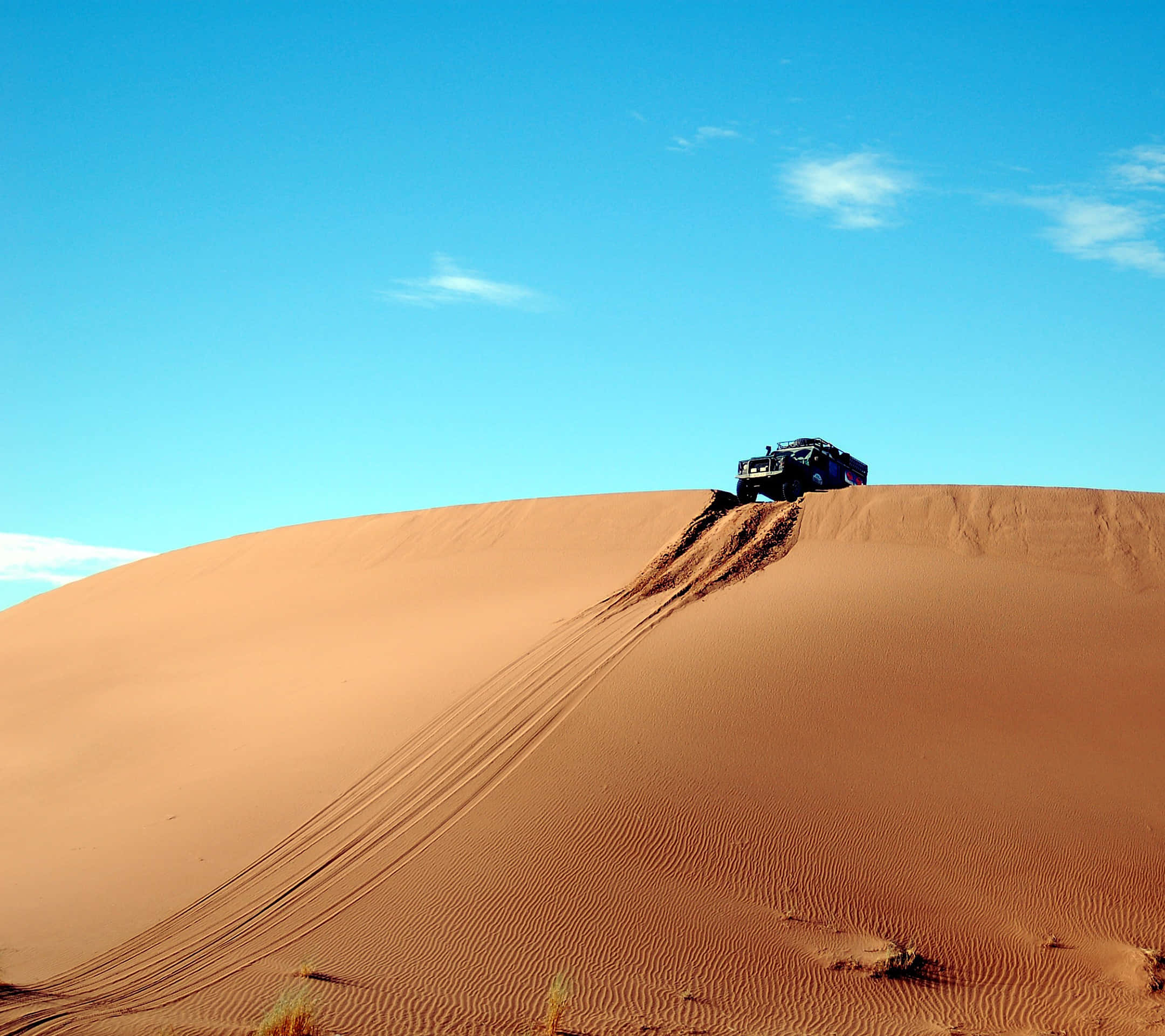 Sand Dunes 桌布 壁紙 — 一輛堅固的越野車在廣闊清澈的藍天下征服高聳的橙色沙丘。