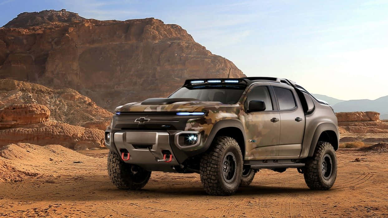 Pick Up Truck 桌布 壁紙 — 一輛堅固的迷彩雪佛蘭 Colorado ZR2 皮卡車配備 LED 燈，停放在廣闊岩石峽谷下塵土飛揚的沙漠小徑上。