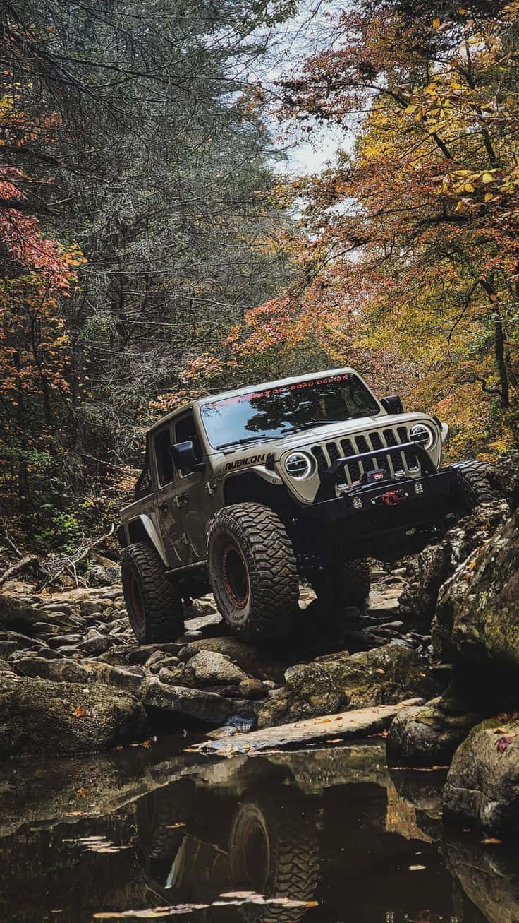 Off-road Car 桌布 壁紙 — 一輛堅固的銀色Jeep Rubicon在色彩繽紛的秋葉和下方倒映水窪的秋日森林中征服岩石地形。
