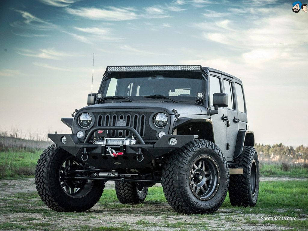 吉普 桌布 壁紙 — 一輛堅固的黑色Jeep Wrangler，配備超大輪胎和車頂燈條，矗立在多雲天空下的草地上。