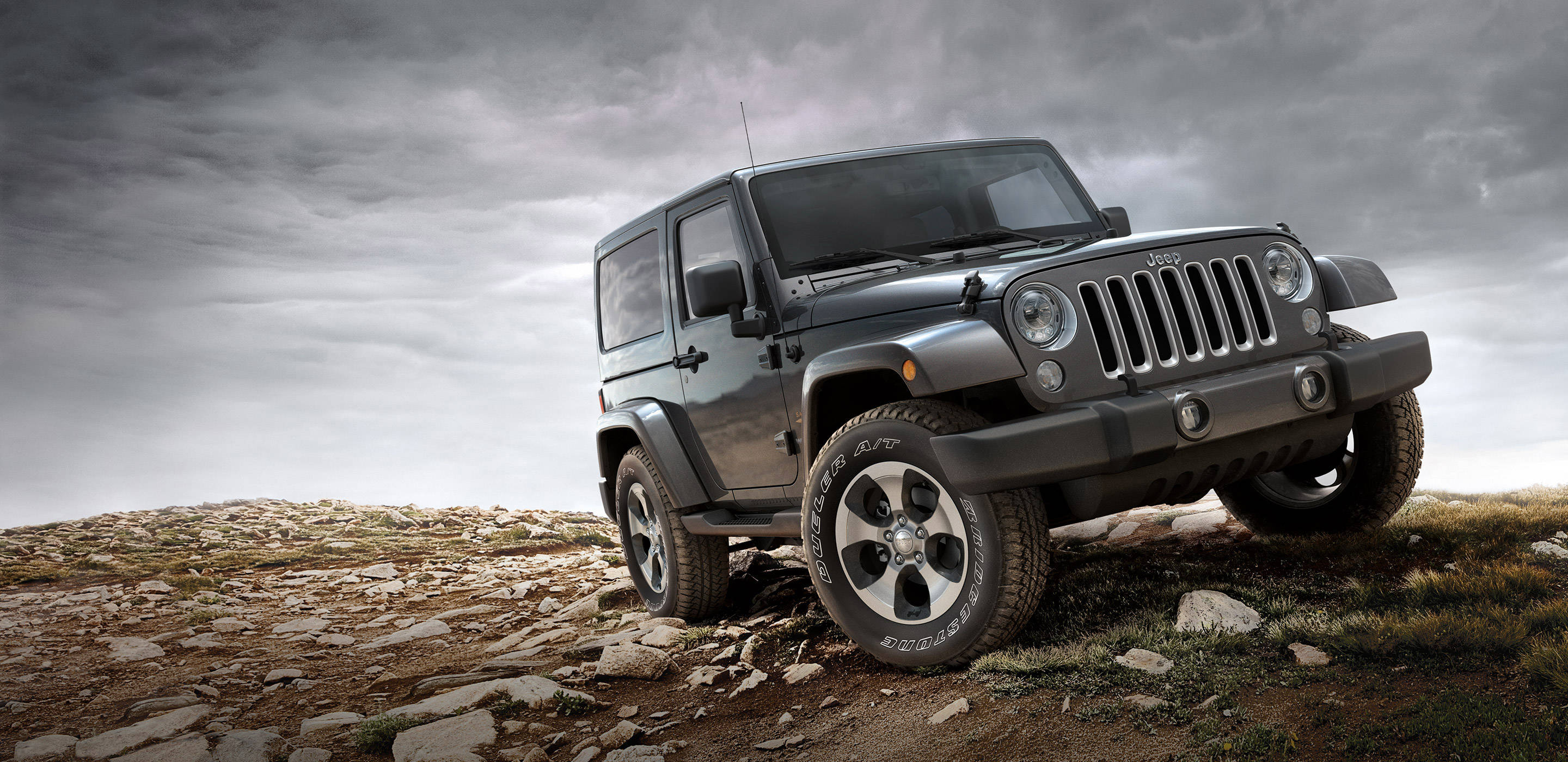 Wrangler 桌布 壁紙 — 一輛堅固的黑色Jeep Wrangler在戲劇性的陰天下，矗立在岩石山坡上。