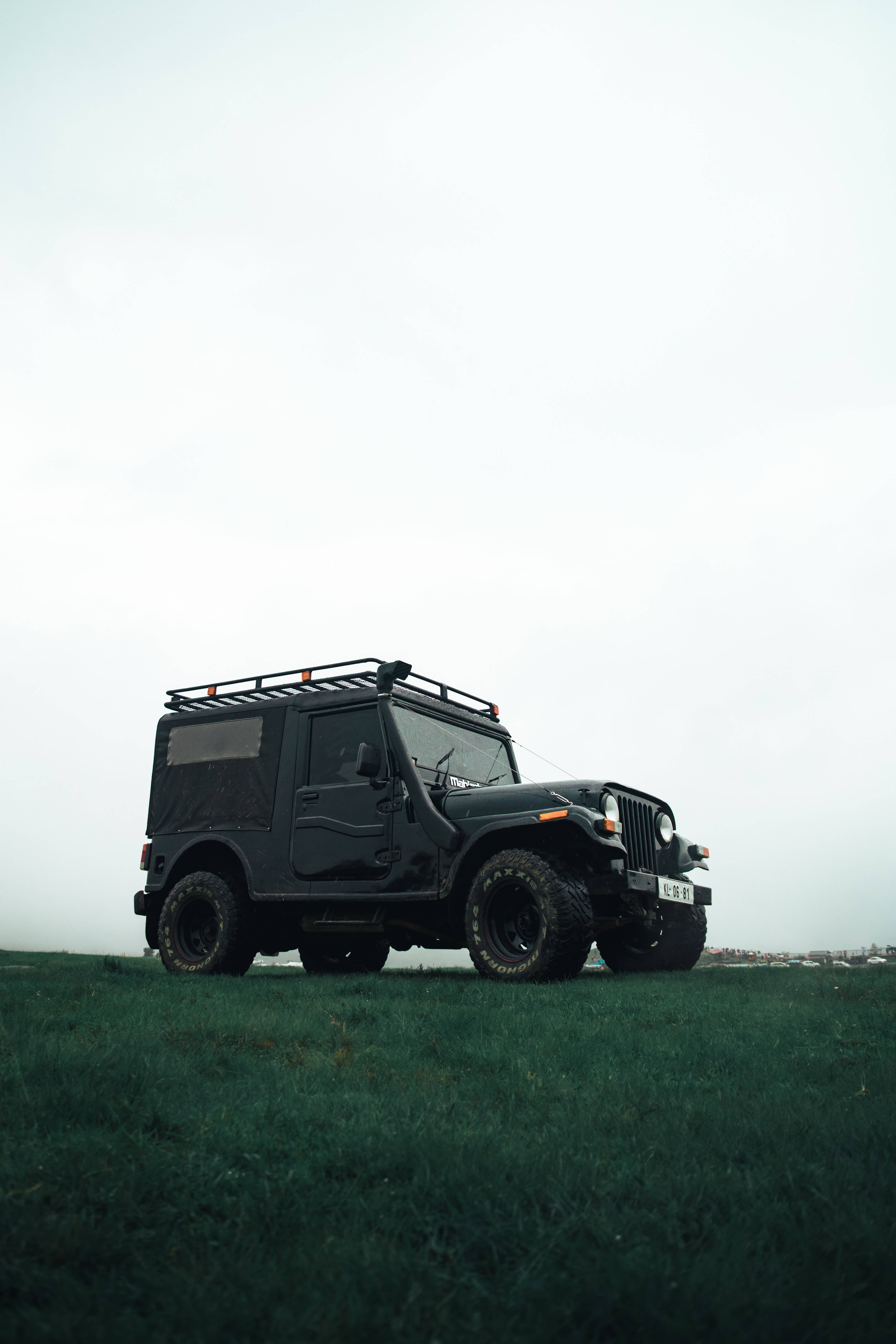 Grass 桌布 壁紙 — 一輛堅固的黑色吉普車配備車頂行李架，獨自停泊在陰天下一片霧氣瀰漫的綠色山丘上。