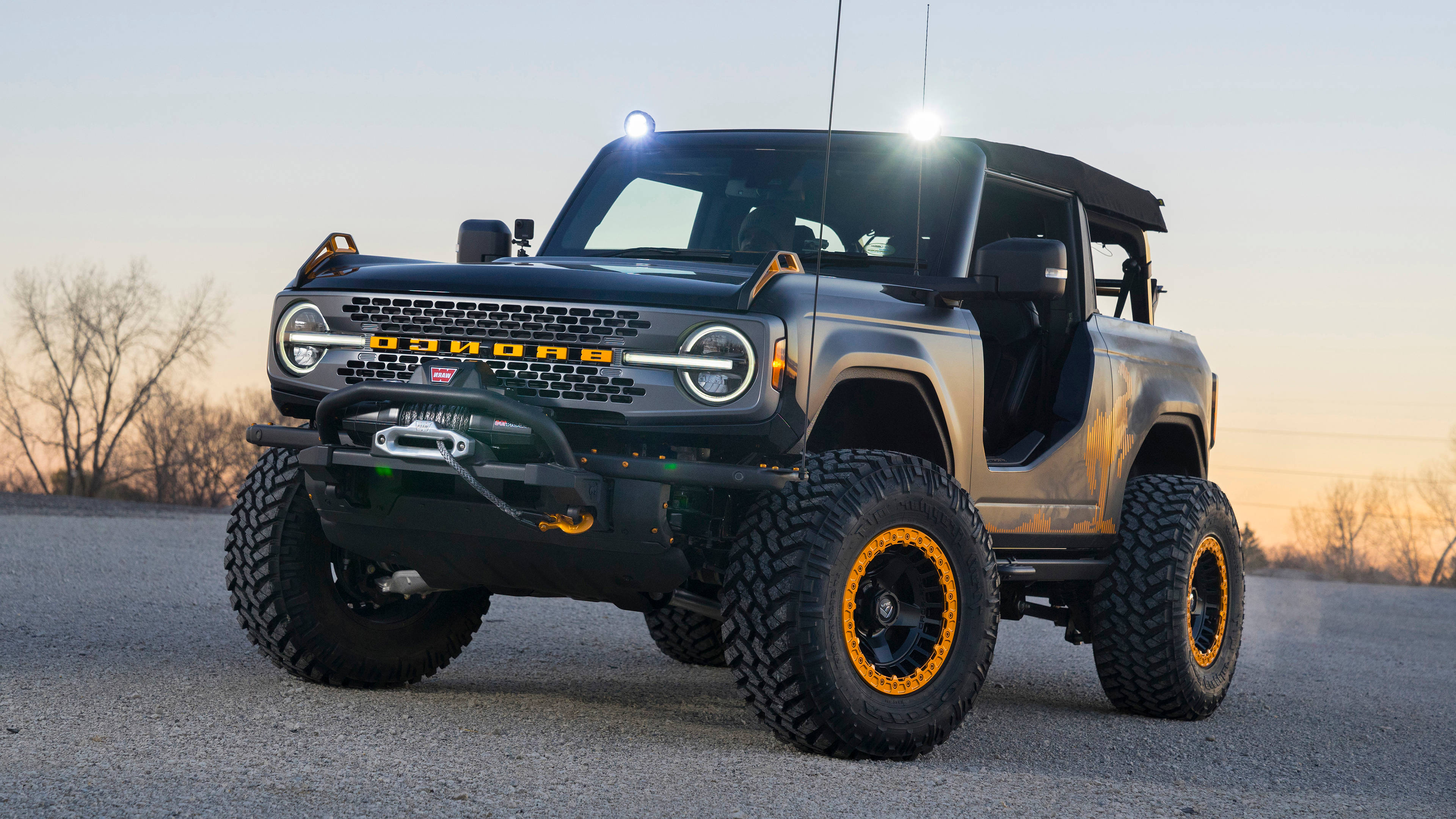 Ford Bronco 桌布 壁紙 — 一輛堅固的黑色福特Bronco，帶有橙色輪圈，在日落時分停在碎石路上。