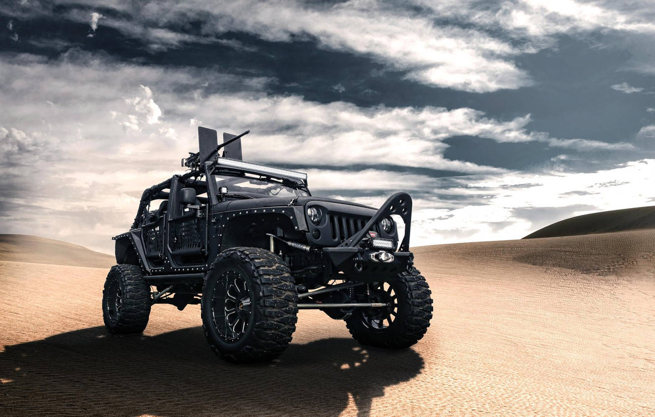 Wrangler 桌布 壁紙 — 一輛堅固的黑色越野車矗立在金色沙漠沙丘上，背景是戲劇性的多雲天空。