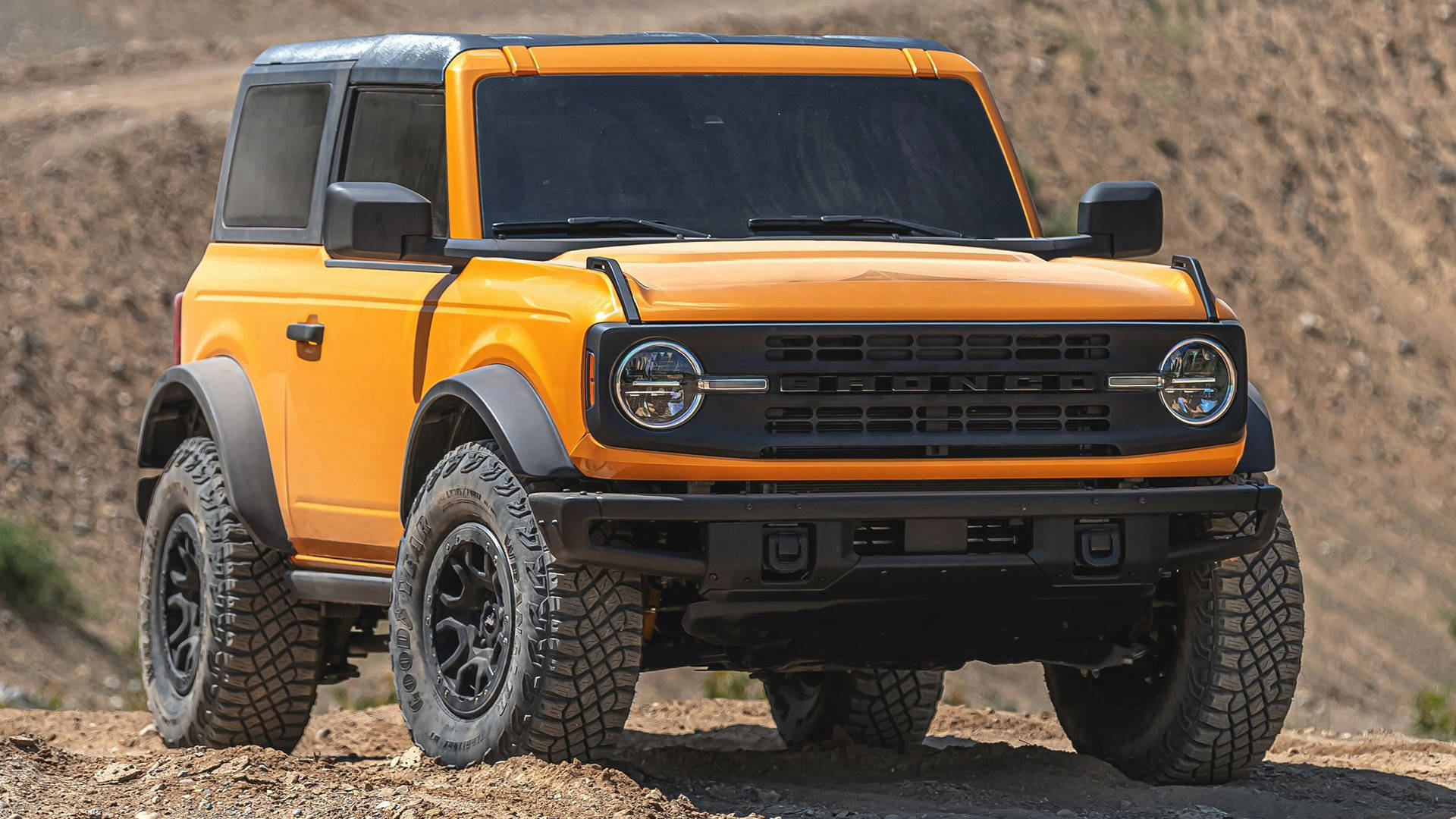 Ford Bronco 桌布 壁紙 — 一輛大膽的橙色福特Bronco SUV，帶有黑色飾邊和堅固輪胎，在明亮的日光下停在岩石沙漠小徑上。