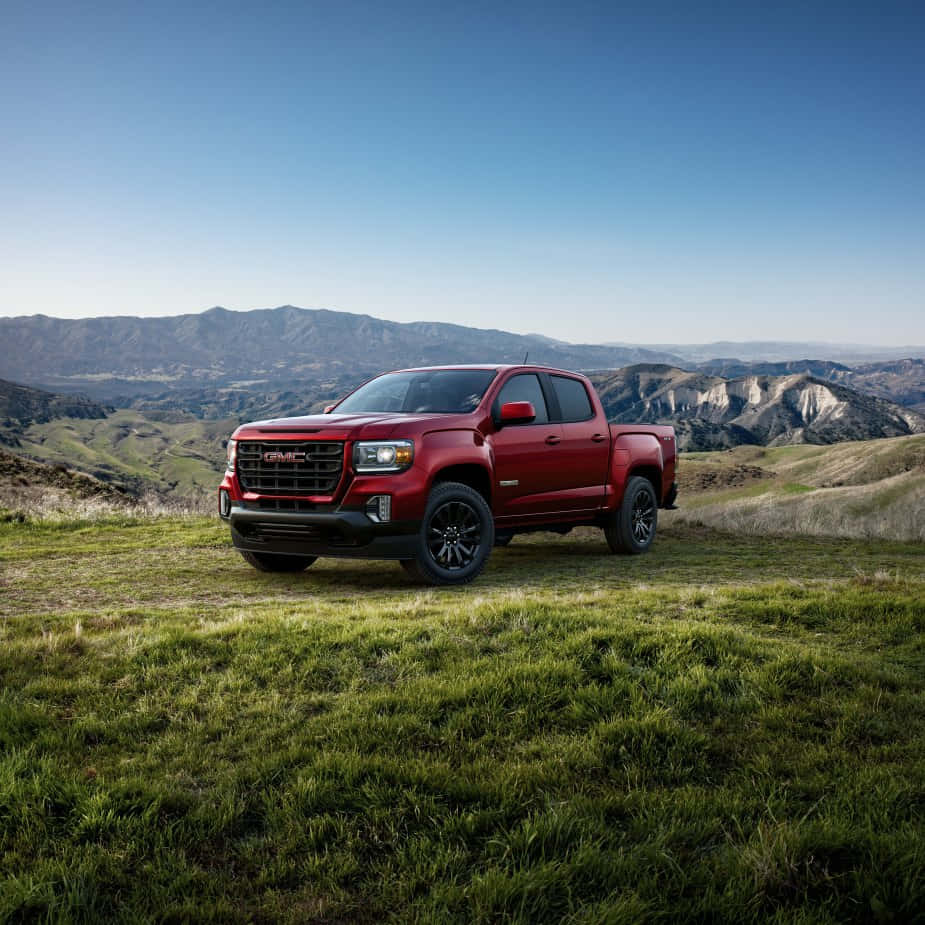 Gmc Canyon 桌布 壁紙 — 一輛大膽的紅色GMC Sierra皮卡車停放在陽光明媚的草地上，俯瞰著連綿起伏的山脈，天空湛藍清澈。