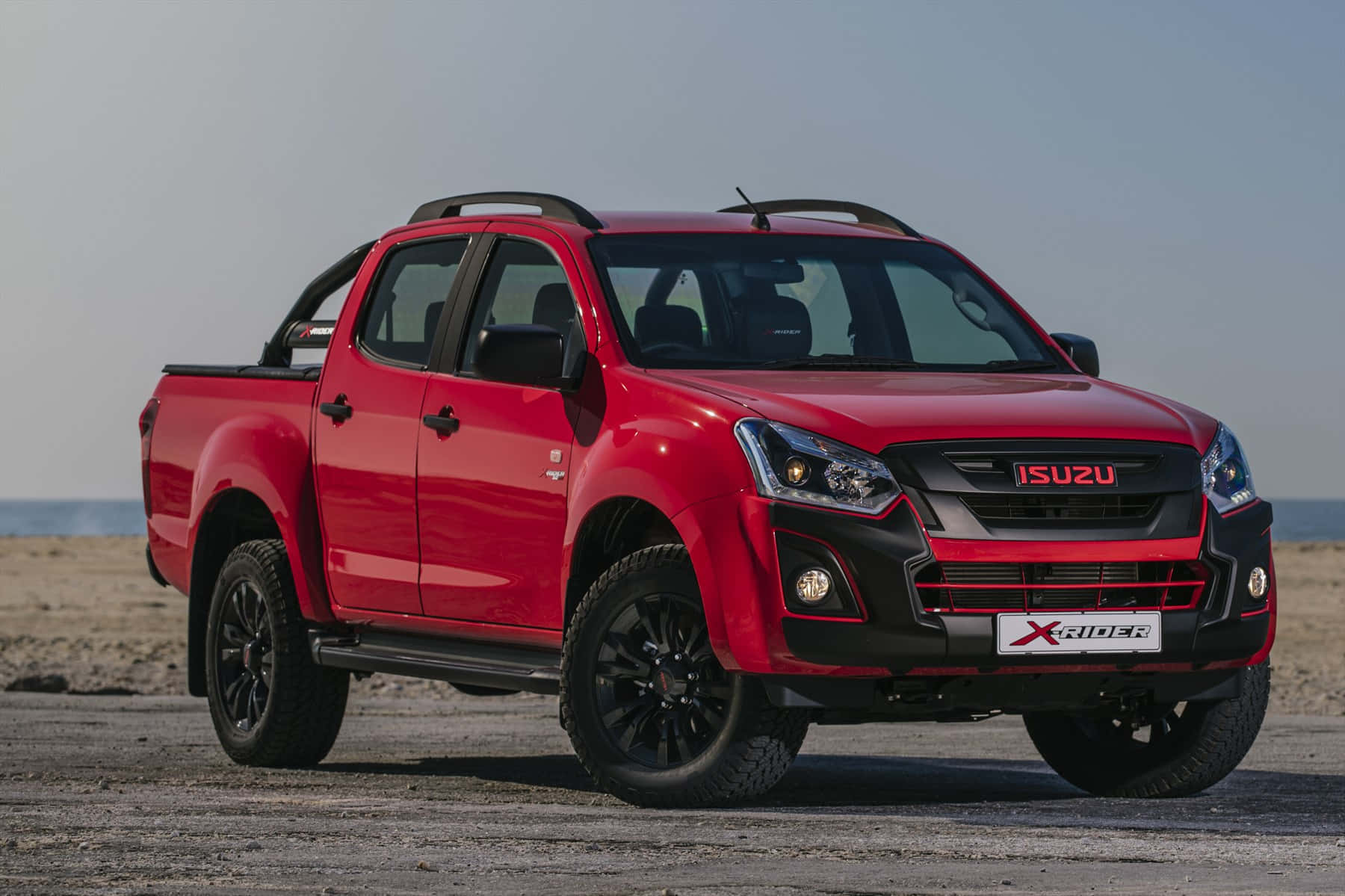 Isuzu 桌布 壁紙 — 一輛大膽的紅色Isuzu X-Rider pickup貨車停泊在陽光明媚的海灘上，背後是海洋地平線。