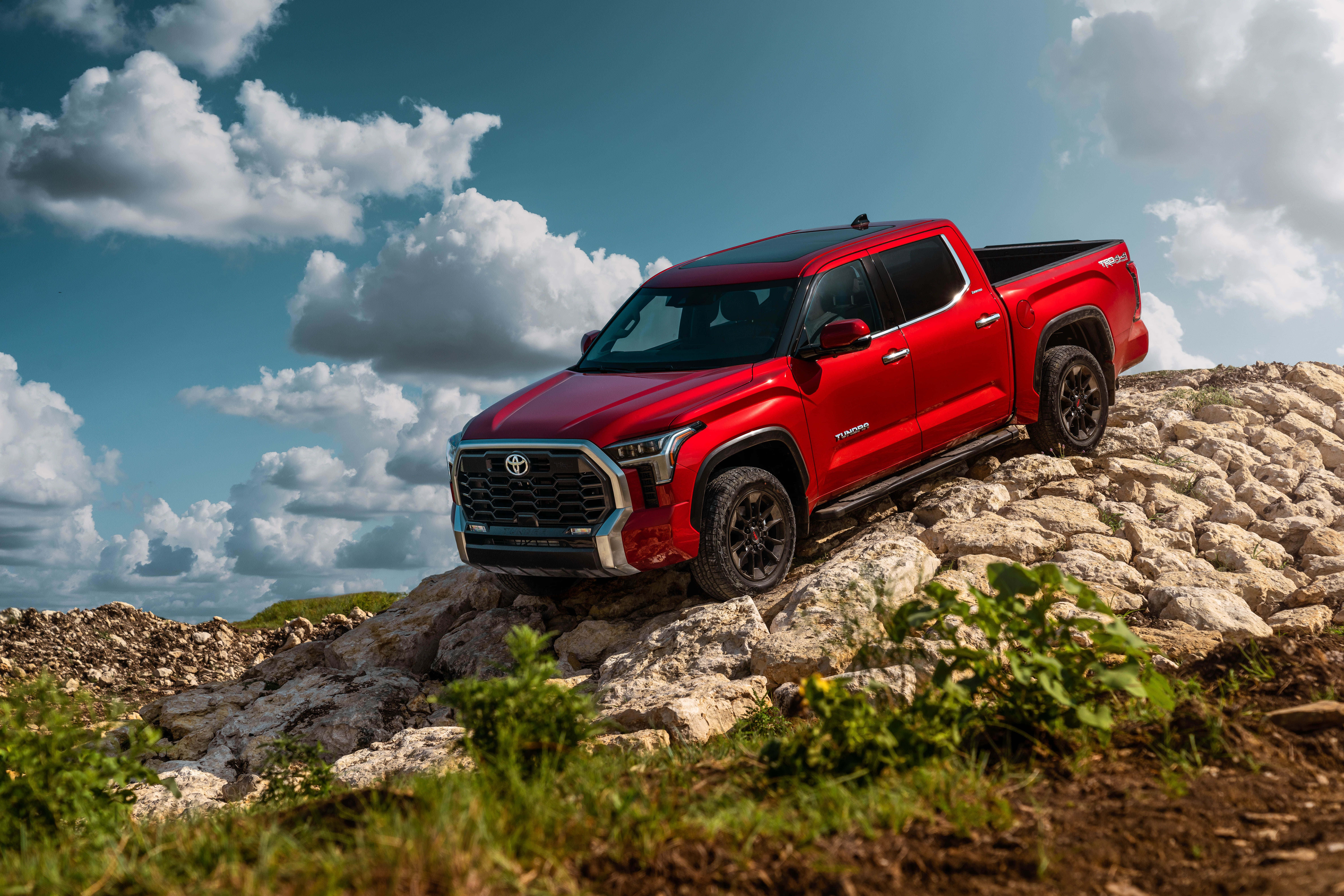 Toyota 桌布 壁紙 — 一輛大膽的紅色豐田 Tacoma 皮卡車在晴朗的藍天和蓬鬆的白雲下征服崎嶇的岩石山丘。