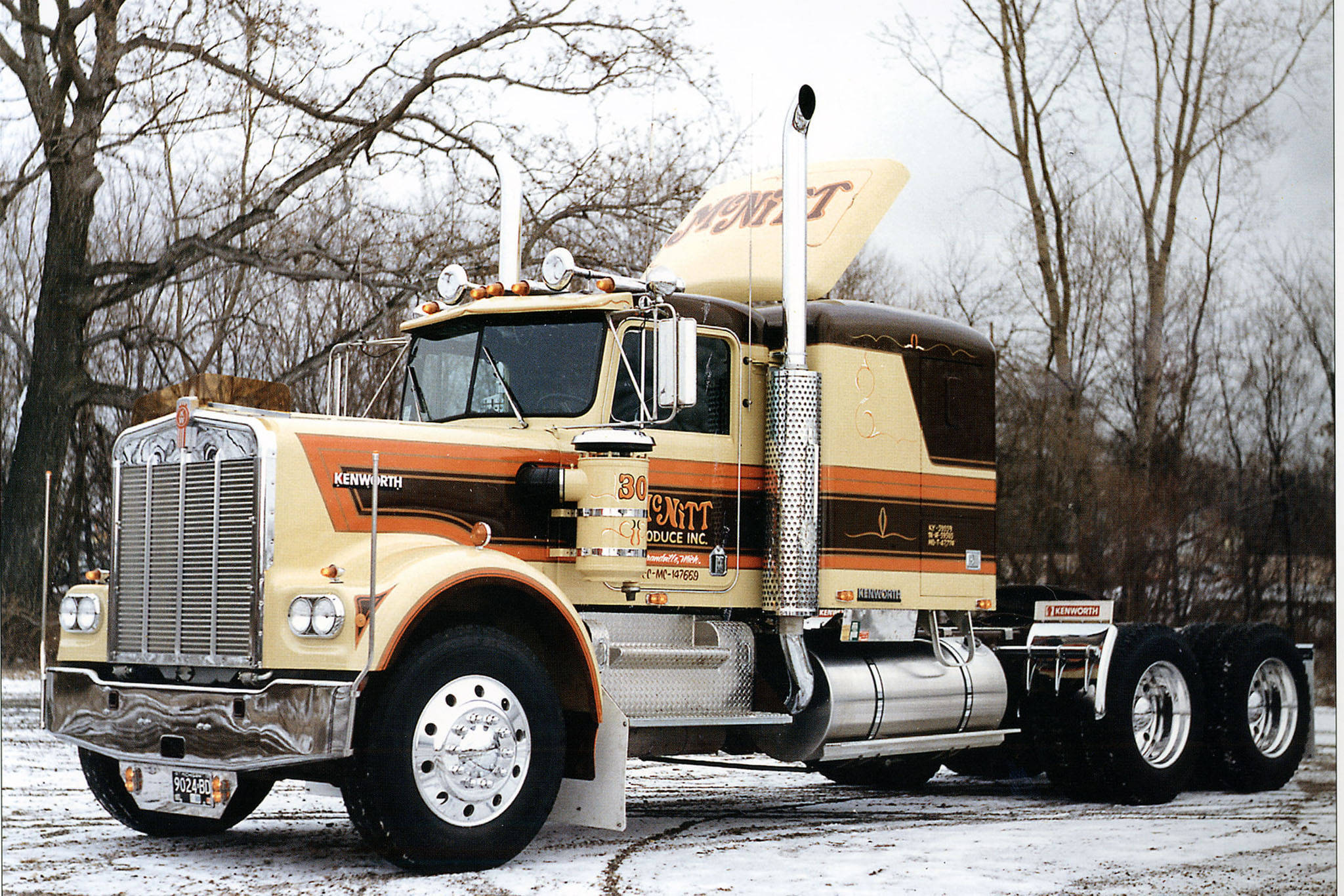 Kenworth W900 桌布 壁紙 — 一輛奶油色和棕色的經典Kenworth半掛卡車，帶有鍍鉻裝飾，停在白雪覆蓋的森林空地上。