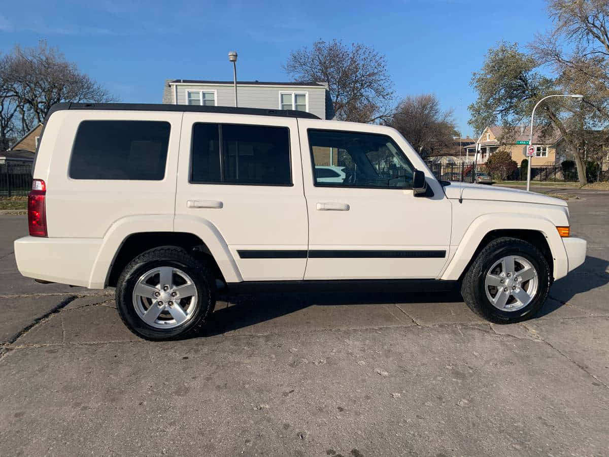 Jeep Commander 桌布 壁紙 — 一輛奶油色的Jeep Commander SUV停放在破裂的柏油路上，背景是晴朗的藍天、光禿的樹木和郊區房屋。
