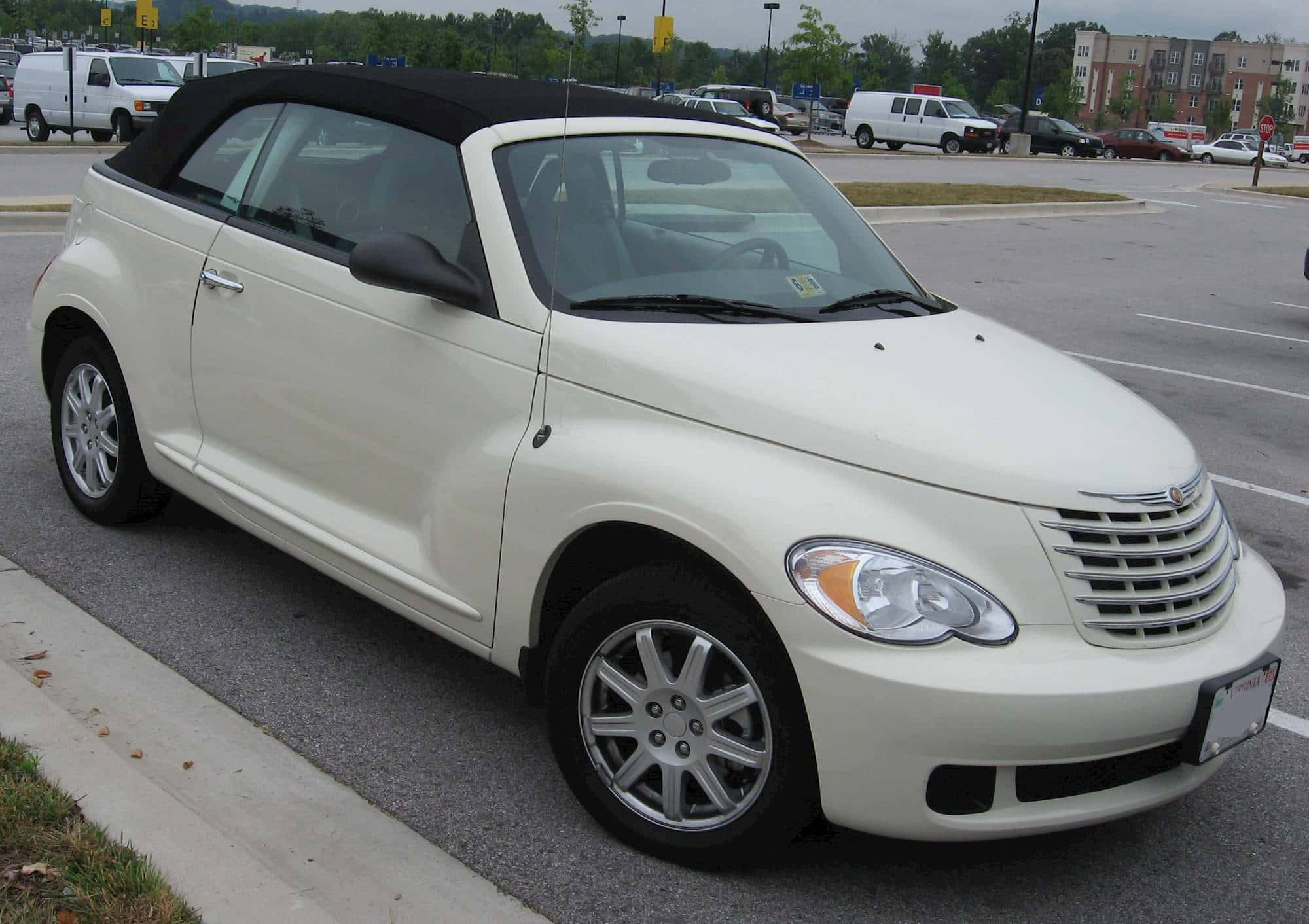 Chrysler Pt Cruiser 桌布 壁紙 — 一輛奶油色的PT Cruiser敞篷車停放在鋪砌的停車場，背景有樹木和建築物。