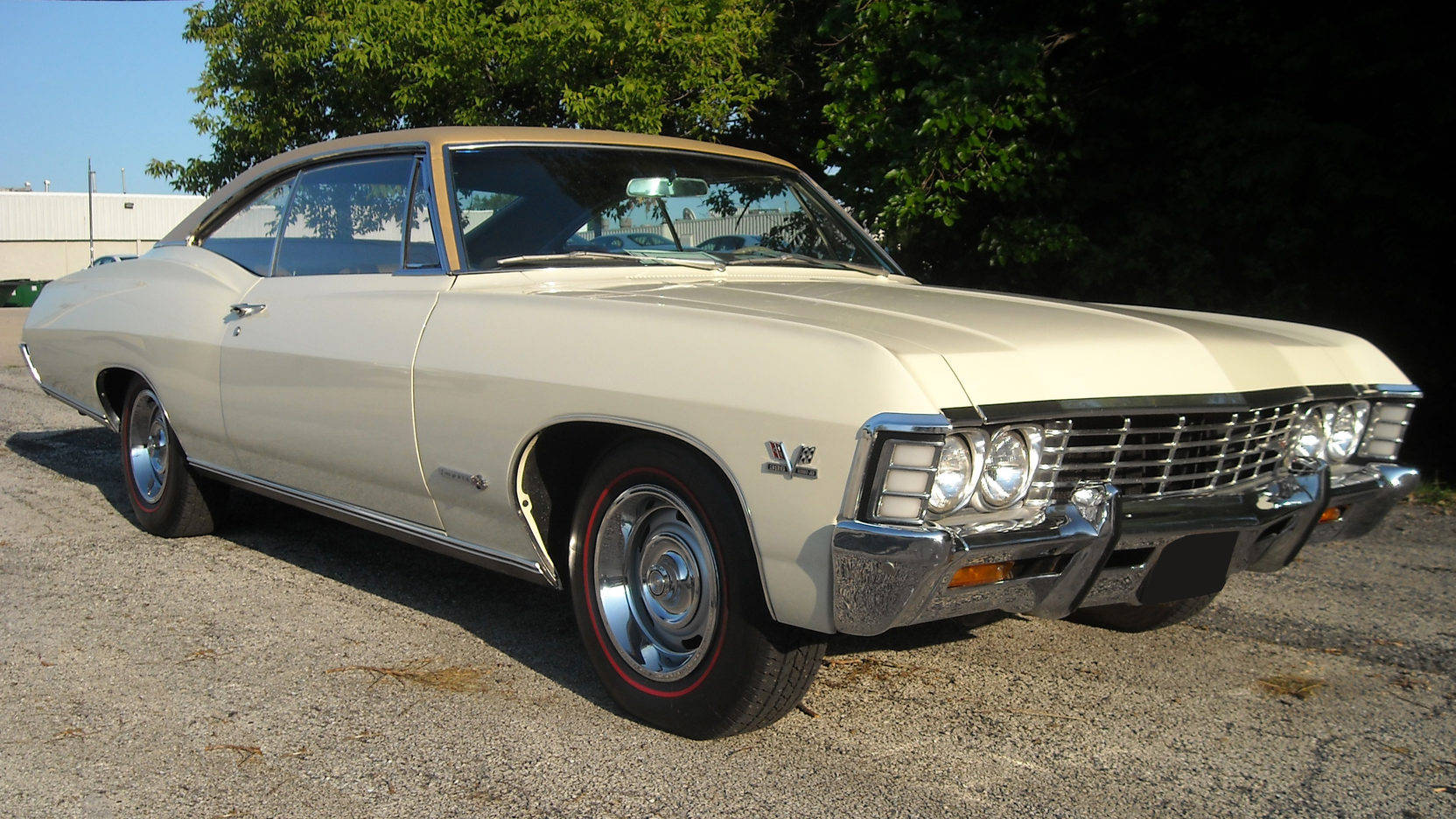chevrolet impala 1967 桌布 壁紙 — 一輛奶油色經典肌肉車，帶有鍍鉻裝飾和紅線輪胎，停在明亮的日光下的礫石上。