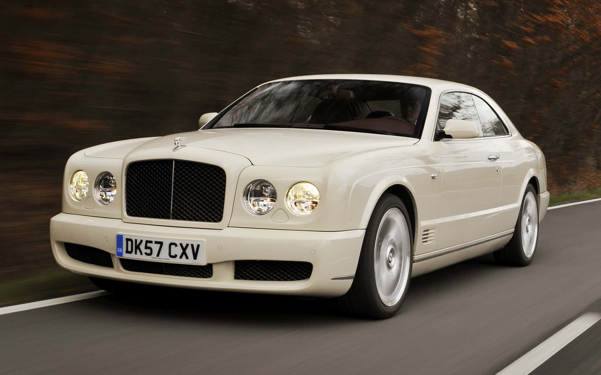 Bentley Brooklands 桌布 壁紙 — 一輛奶油色賓利 Continental GT 在道路上疾馳，背景是模糊的秋樹。