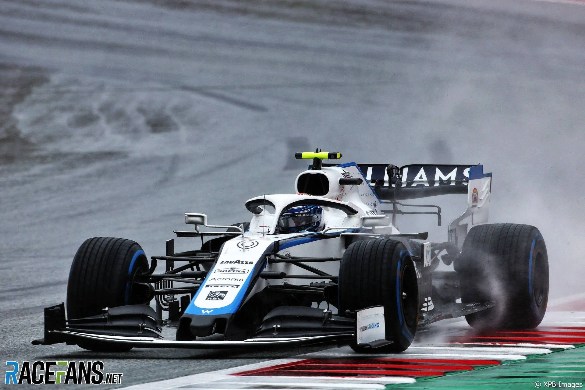 F1 桌布 壁紙 — 一輛威廉斯一級方程式賽車在潮濕的彎道中高速行駛，在雨水滑溜的賽道上噴出水霧。