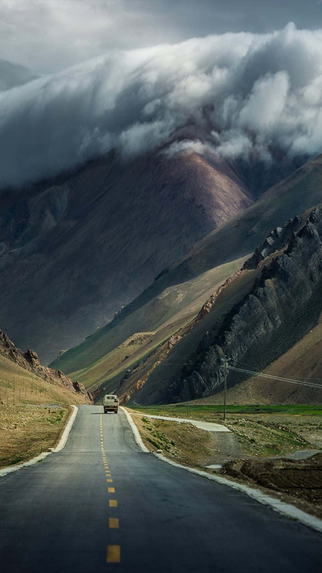 Road 桌布 壁紙 — 一輛孤獨的卡車在戲劇性的雲霧籠罩的山峰下行駛在蜿蜒的山路上。