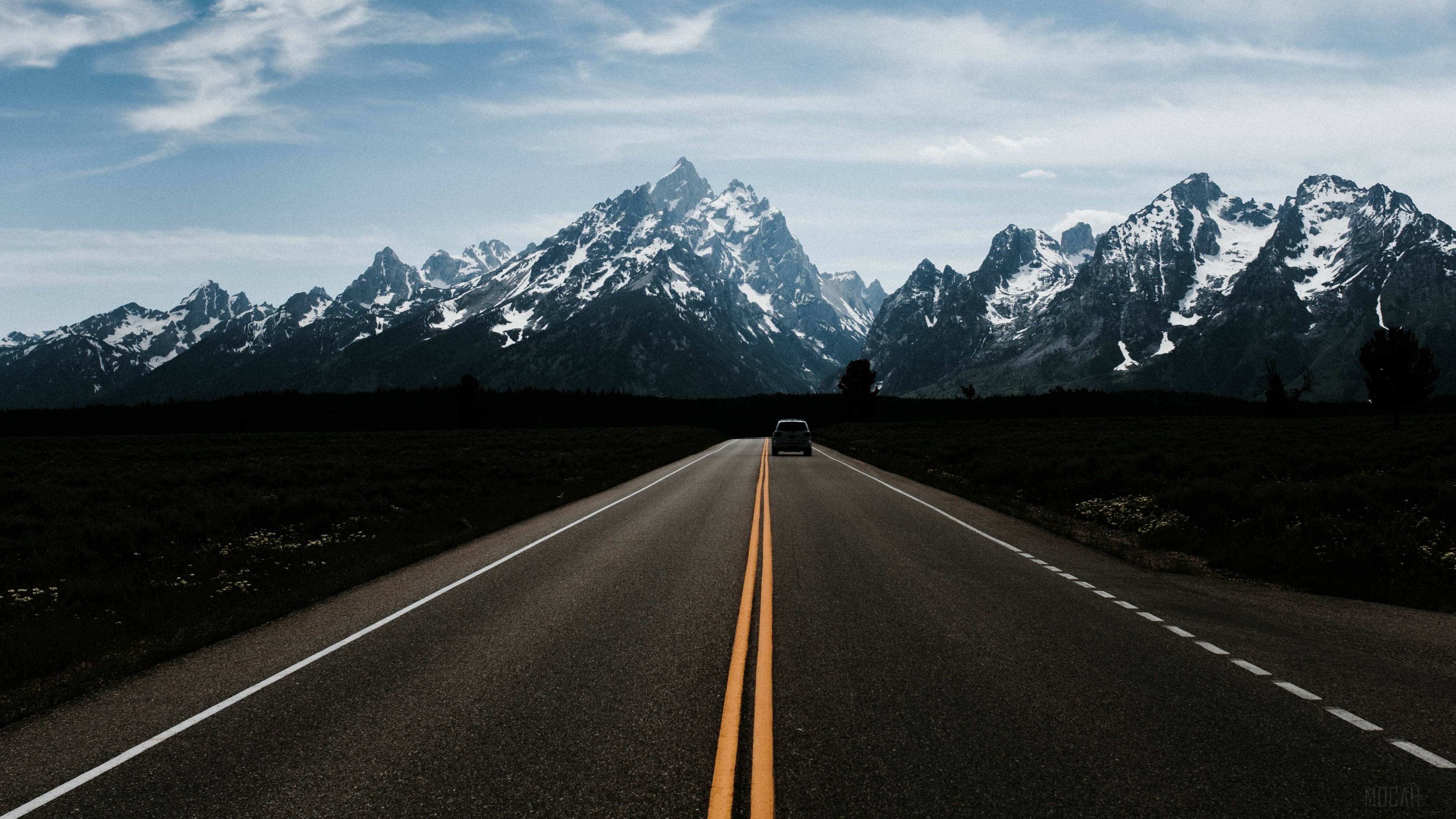 Road 桌布 壁紙 — 一輛孤獨的汽車在陰天下行駛在一條筆直的道路上，朝著積雪的山脈前進。