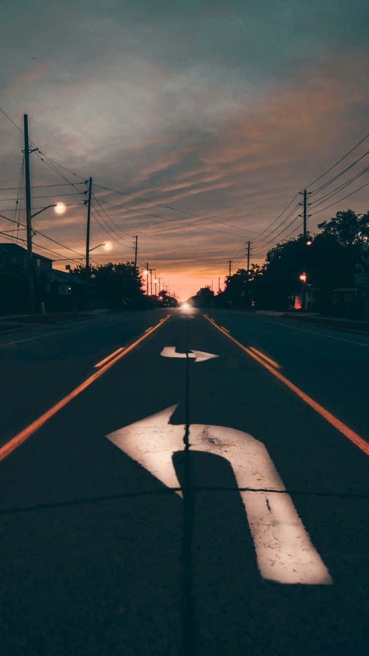 美學 iPhone 壁紙 桌布 壁紙 — 一輛孤獨的汽車的車頭燈劃破暮色，沿著一條兩旁有電線杆和樹木的寧靜郊區街道駛近。