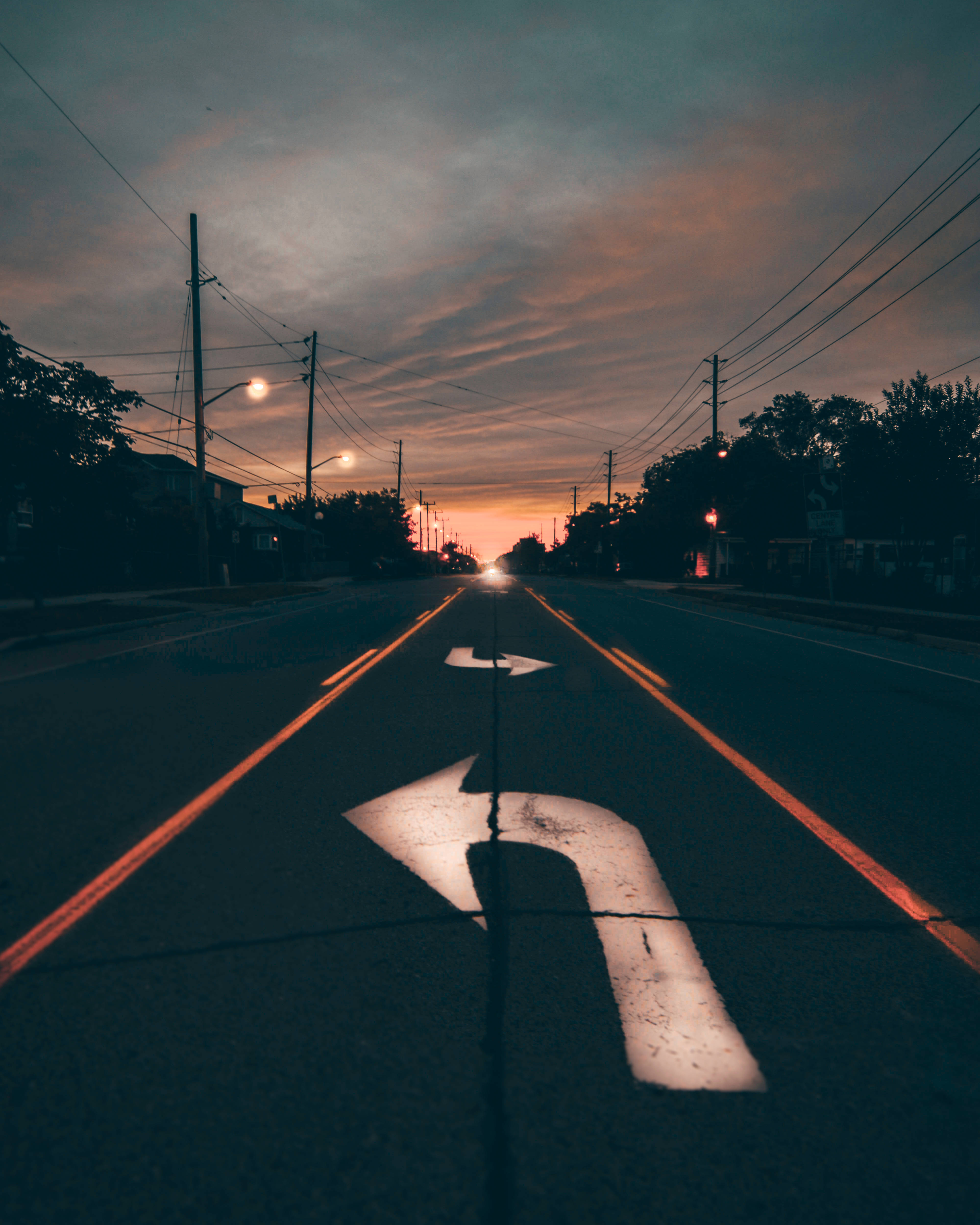 Road 桌布 壁紙 — 一輛孤獨的汽車的車頭燈劃破暮色，行駛在一條兩旁種滿樹木和電線的寧靜郊區街道上。