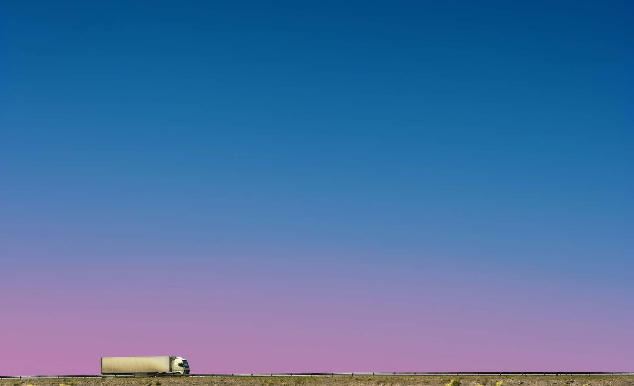 Minimalist Sky 桌布 壁紙 — 一輛孤獨的白色半掛卡車在沙漠高速公路上行駛，頭頂是從深藍色漸變到柔和粉紅色的廣闊天空。